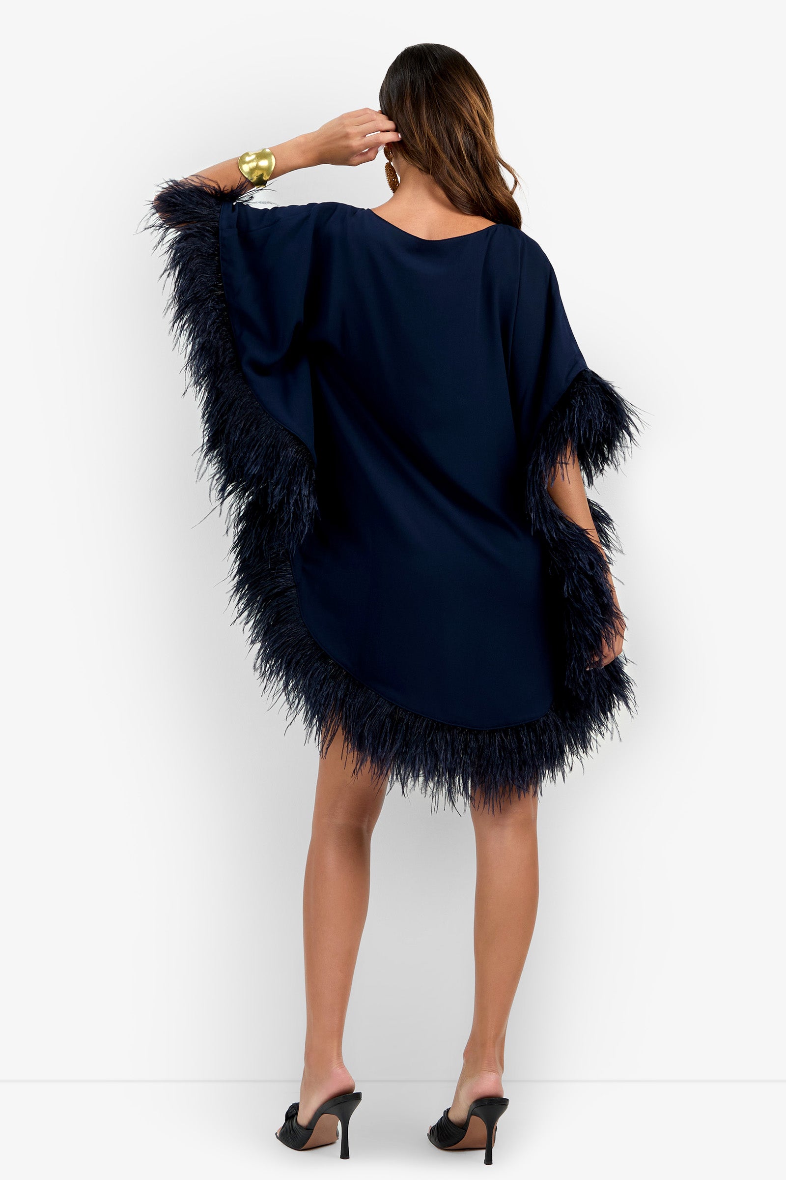 Woman wearing the Mini Neena Fringe Dress in navy blue, styled with black heels, posing with her back to the camera and her hand touching her hair.