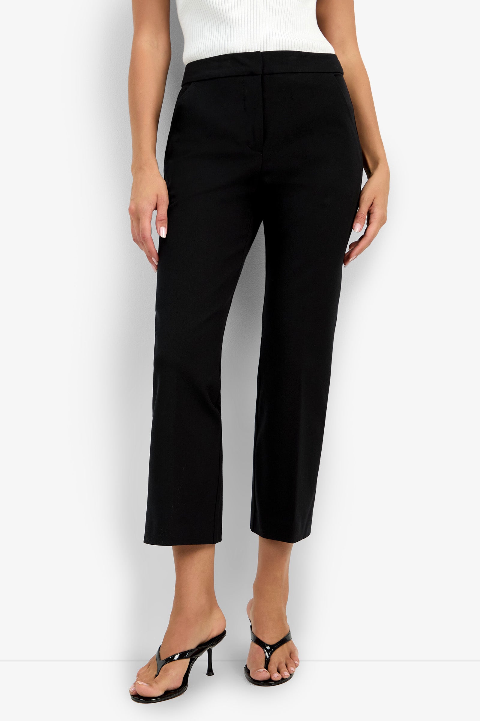 A person wearing the Lulu Pant in black, paired with a white sleeveless top and black open-toe heeled sandals, stands against a white background. Only the lower half of the body is shown.