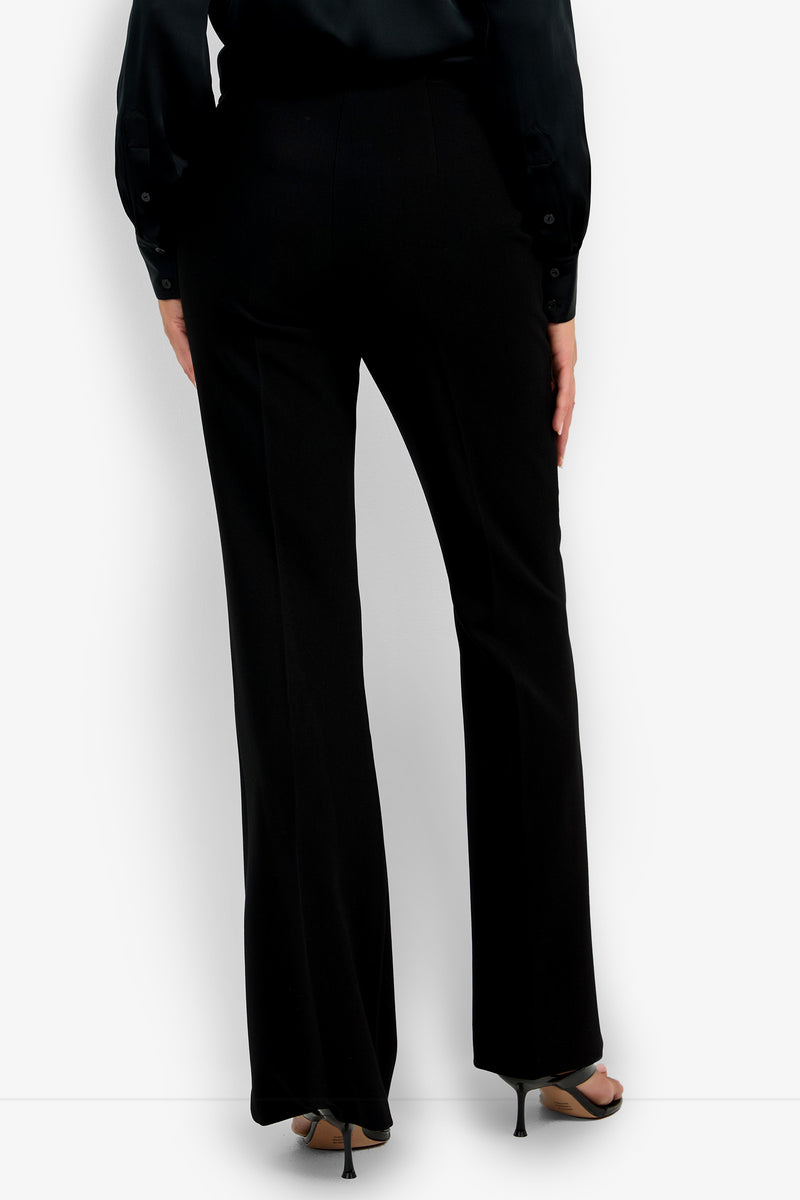 A person is shown from the back wearing the tailored, slightly flared Chimayo Pant in black with black heeled sandals and a black long-sleeve shirt.