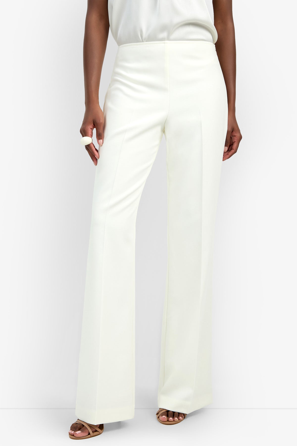 Someone stands against a plain background wearing the Chimayo Pant, which is high-waisted, wide-leg, and white, paired with a white top, brown heeled sandals, and a visible white ring on one hand.