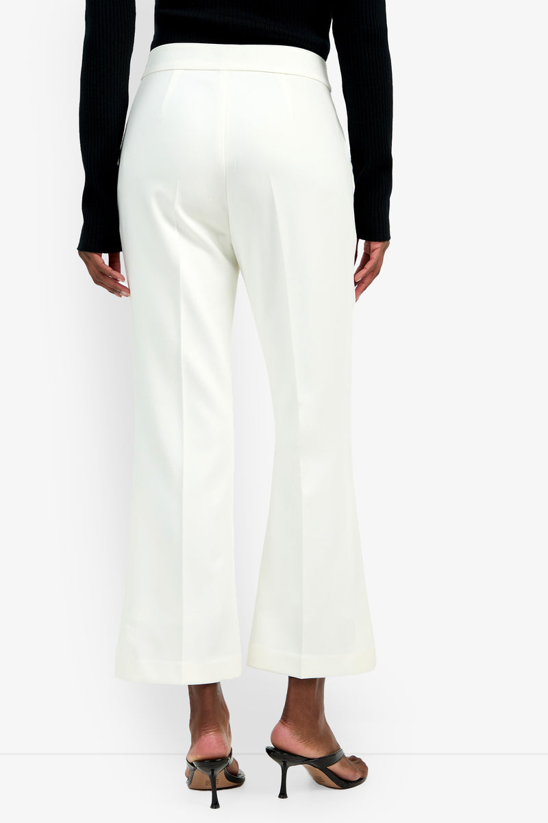 A person faces away against a plain background, wearing the Allisan Pant in white—high-waisted with wide legs—paired with a black ribbed long-sleeve top and black heeled sandals.