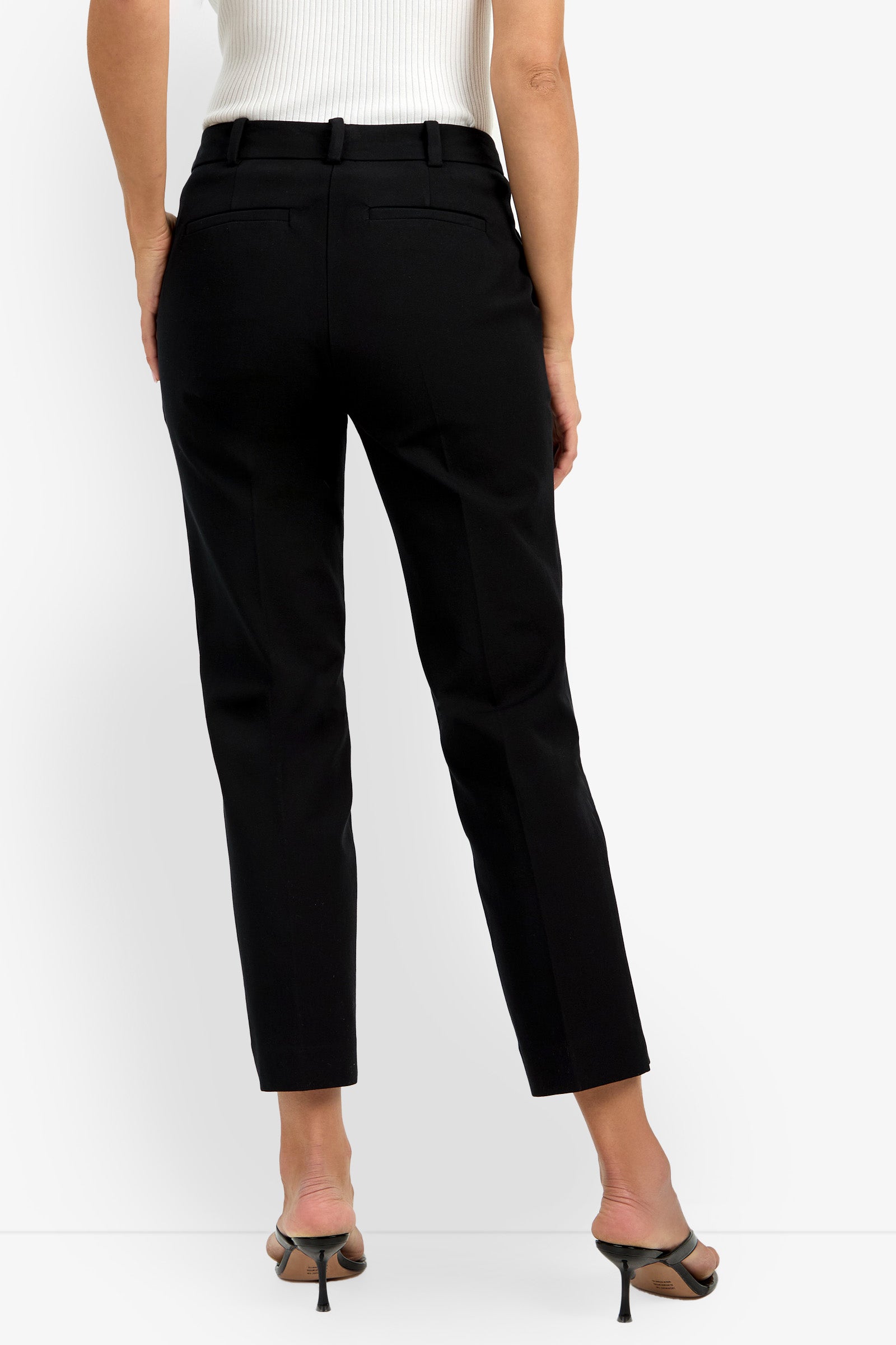 A person is shown from the back wearing the Audrey Pant in black, paired with black heeled sandals and a white sleeveless top against a plain white background.