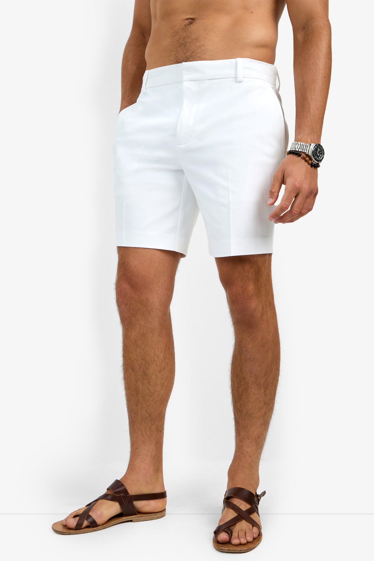 A man stands against a white background, shirtless, with his hands in his pockets. He is wearing the Lawrence Short and brown leather sandals, accessorized with a wristwatch.