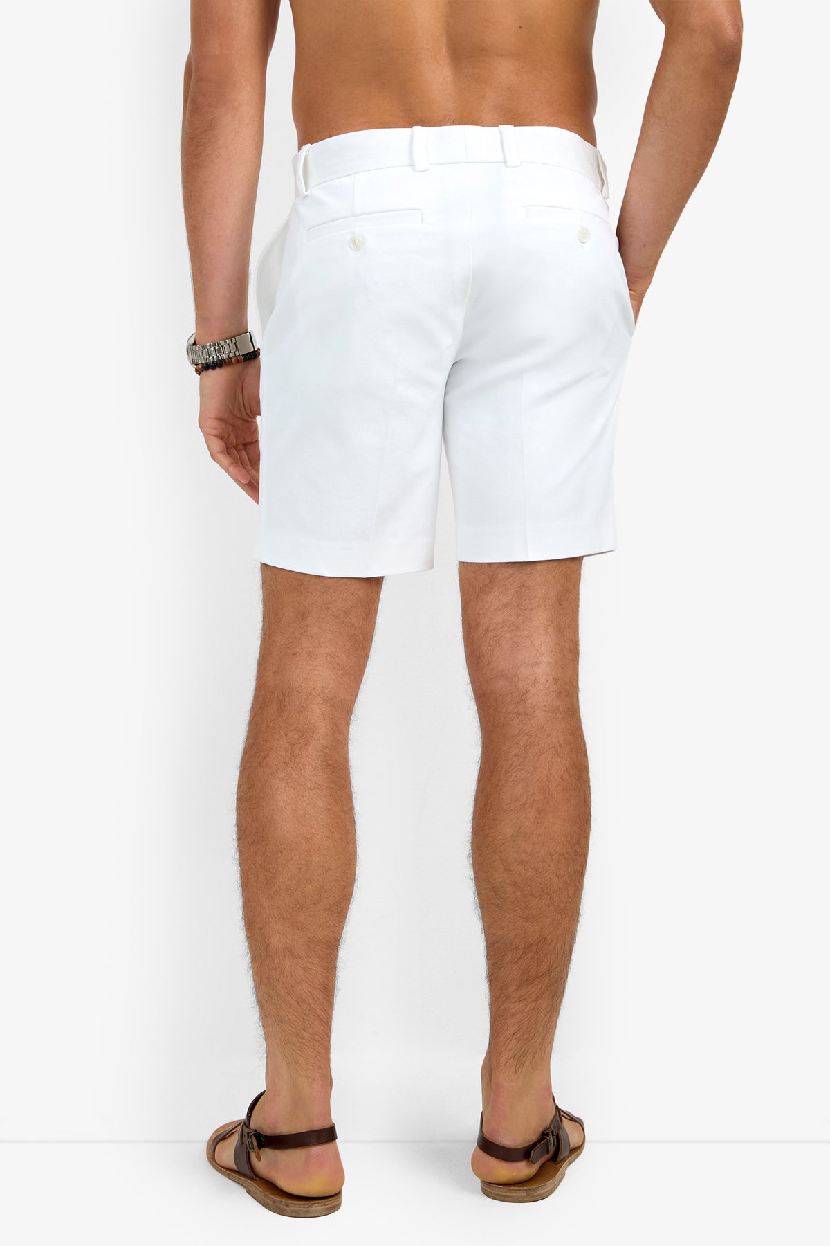 A man is shown from the back, shirtless, wearing the Lawrence Short in white along with brown sandals and a watch, standing against a plain white background.