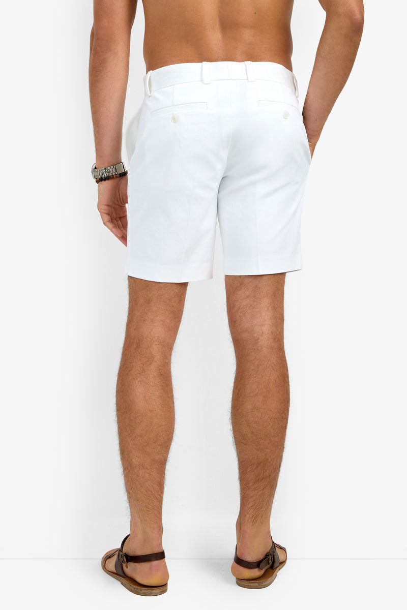 A man is shown from the back, shirtless, wearing the Lawrence Short in white along with brown sandals and a watch, standing against a plain white background.