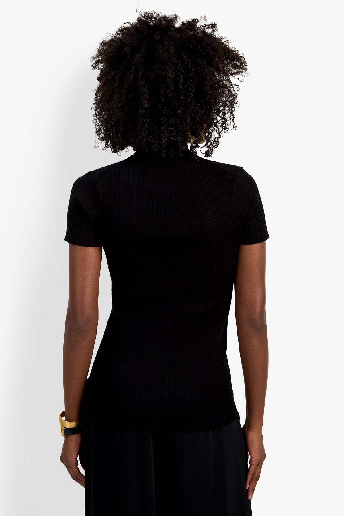 A person with curly hair, wearing the Armeni Mock Neck Top and a gold bracelet, stands facing away from the camera against a plain white background.