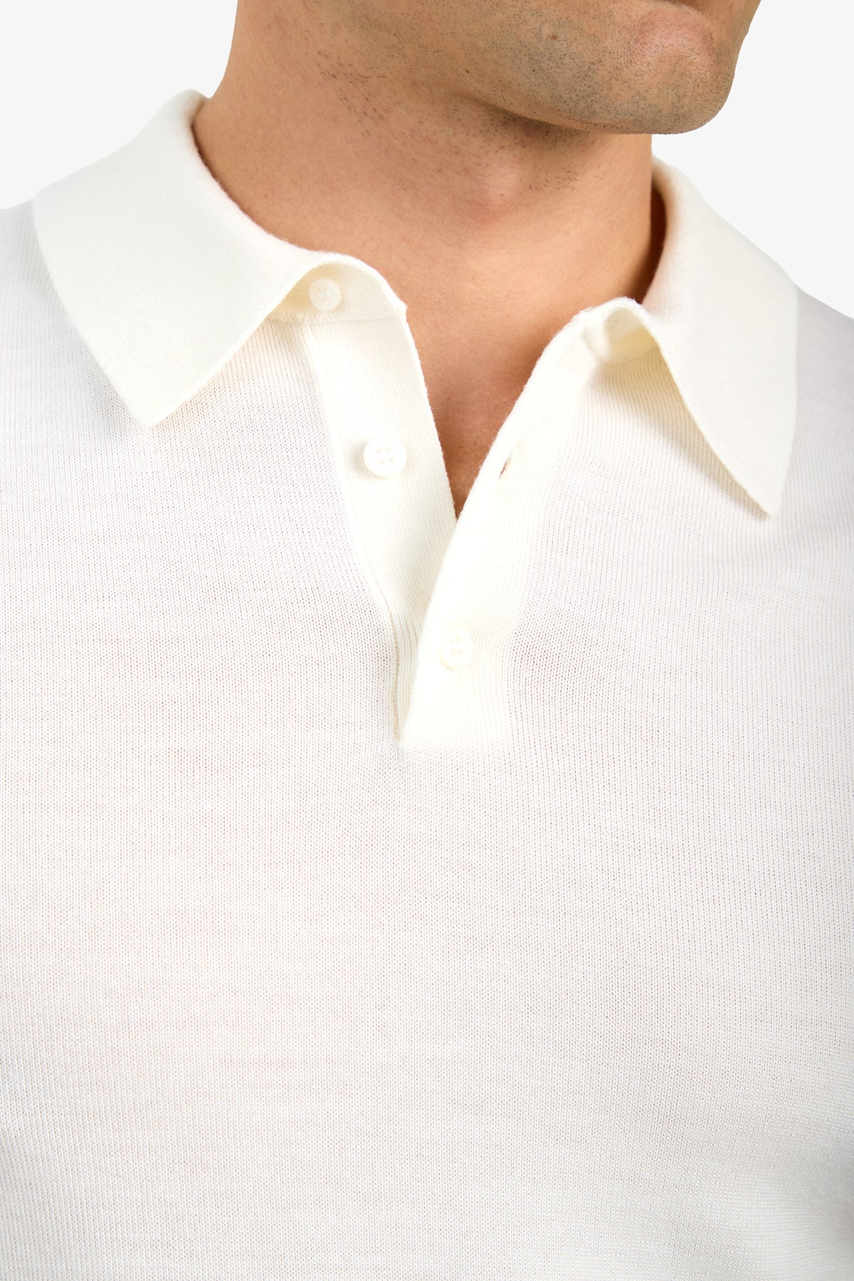 Close-up of a person wearing the Grant Short Sleeve Polo, a cream-colored, collared knit shirt with three buttons. The image shows the upper chest, neck, and part of the lower face against a plain white background.