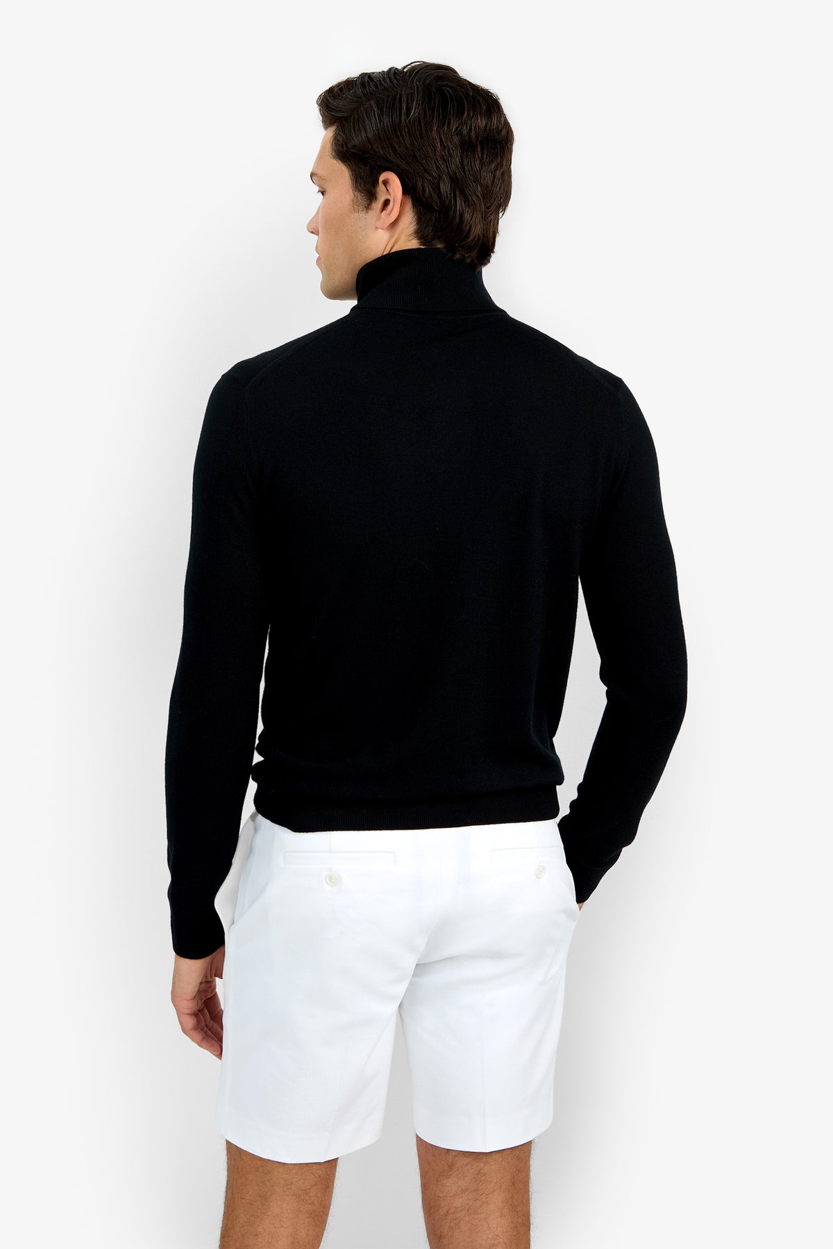 A man with short brown hair stands facing away, wearing the Roy Long Sleeve Turtleneck in black and white shorts. His right arm rests by his side against a plain white background.