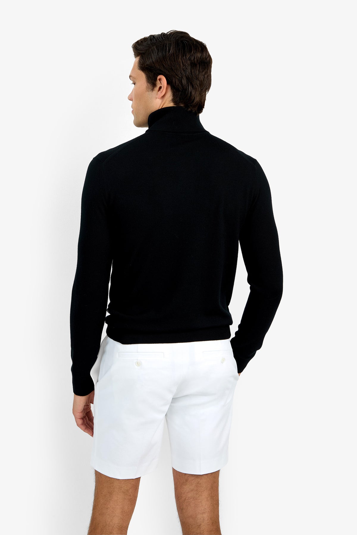 A man faces away from the camera, modeling the Roy Long Sleeve Turtleneck in black with white shorts against a plain white background.
