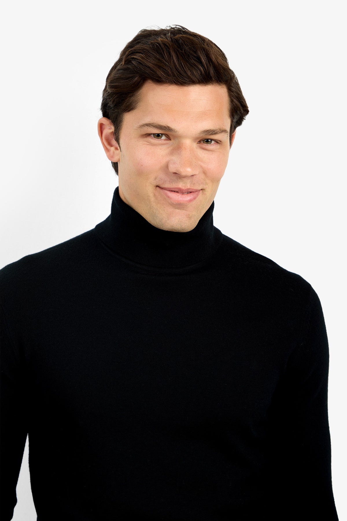 A man with short brown hair softly smiles while wearing the Roy Long Sleeve Turtleneck, standing against a plain white background.