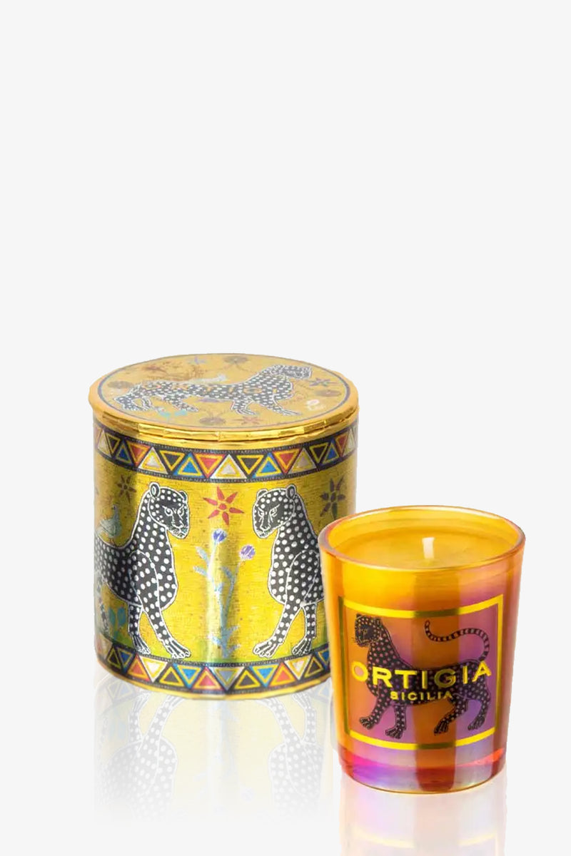 A decorative yellow tin with black and white leopards and floral motifs sits next to the Ortigia Small Candle—an orange glass holder featuring a black leopard design and labeled "Ortigia Sicilia.