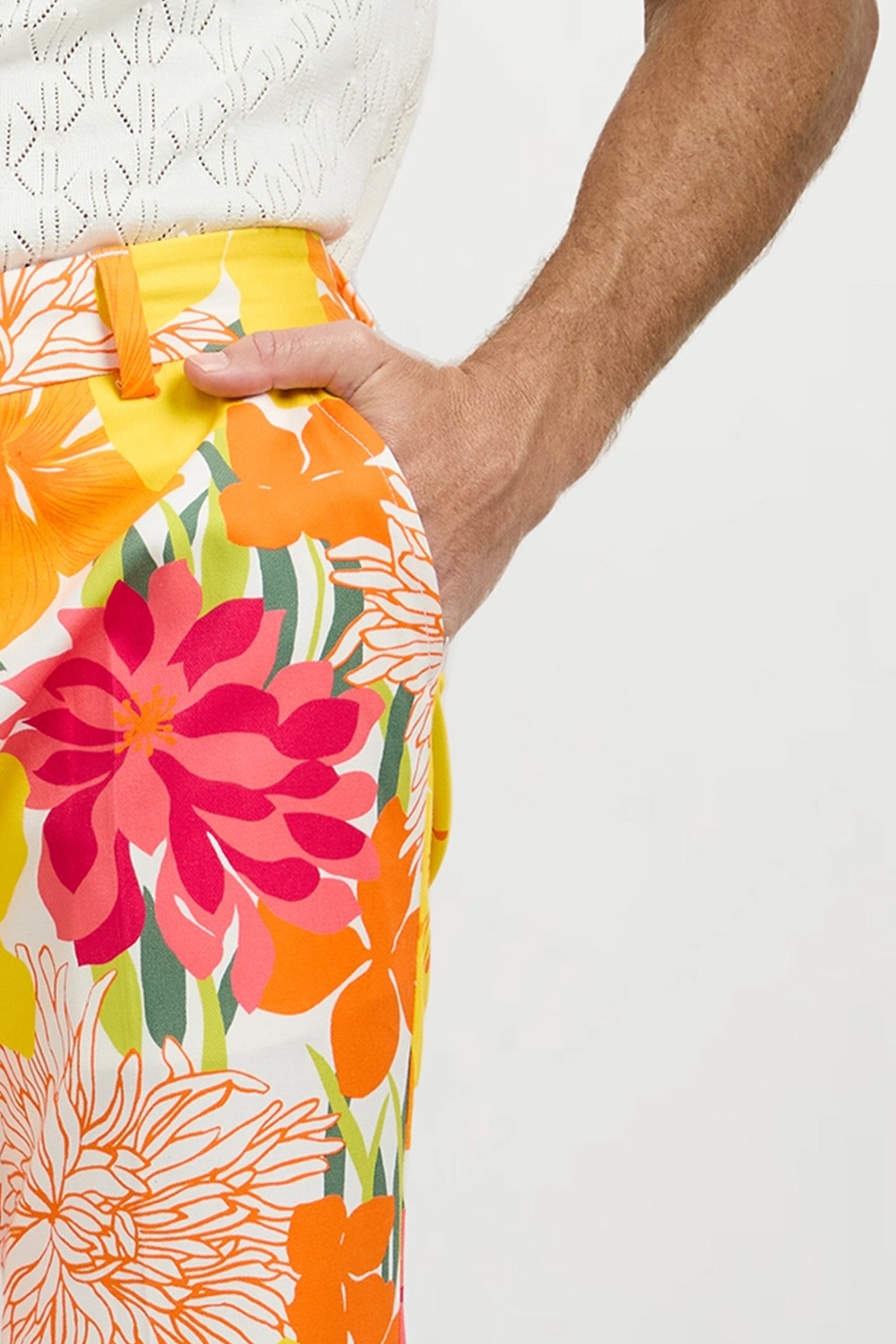 A person wearing a white patterned top and Clyde Slim Trouser - Como Herringbone, standing with their right hand in their pocket against a plain background.