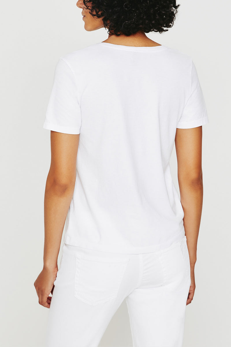 A person with short curly hair is shown from the back, wearing the AG Jager Vee Tee in white and white pants, standing against a plain white background.
