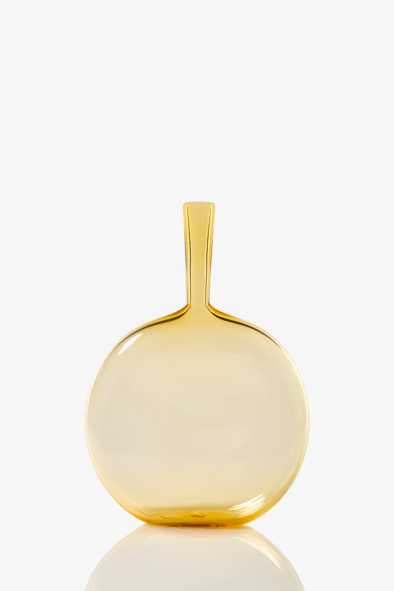 The Flask Angelic Bottle is a round, transparent yellow glass vase with a narrow, straight neck and smooth glossy finish. Its modern, minimalist design stands out elegantly against a plain white background.