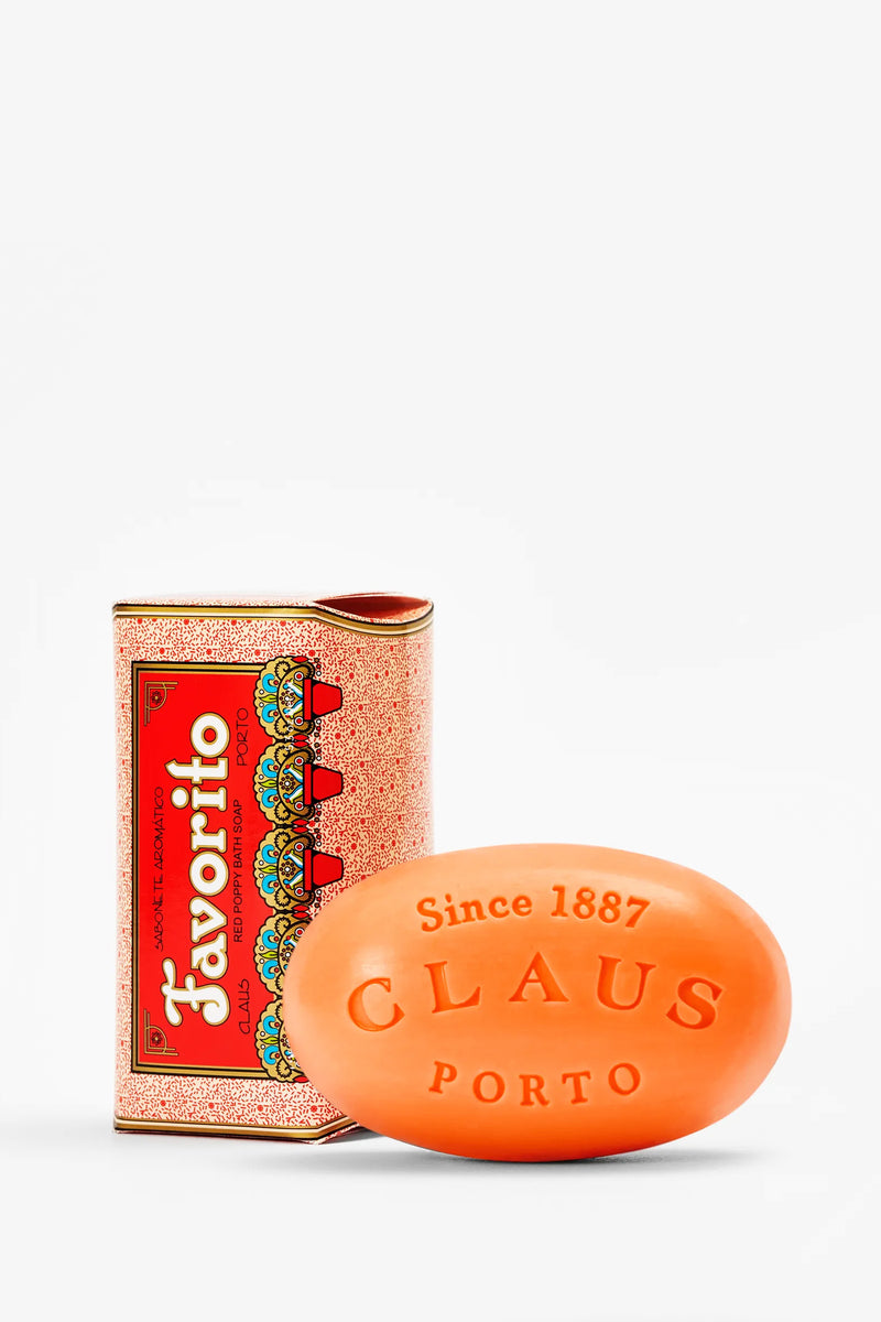 A vibrant orange bar of Claus Porto Favorito Soap, embossed with “Since 1887 CLAUS PORTO,” is displayed beside its ornate red and gold Favorito box.