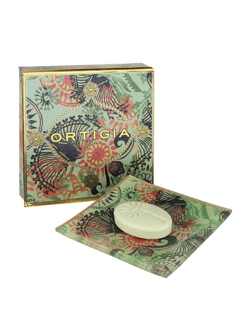 The Ortigia Fico D'India Soapplate features a green, oval embossed soap bar in a matching glass soap dish with a colorful patterned box, all set against a white background.