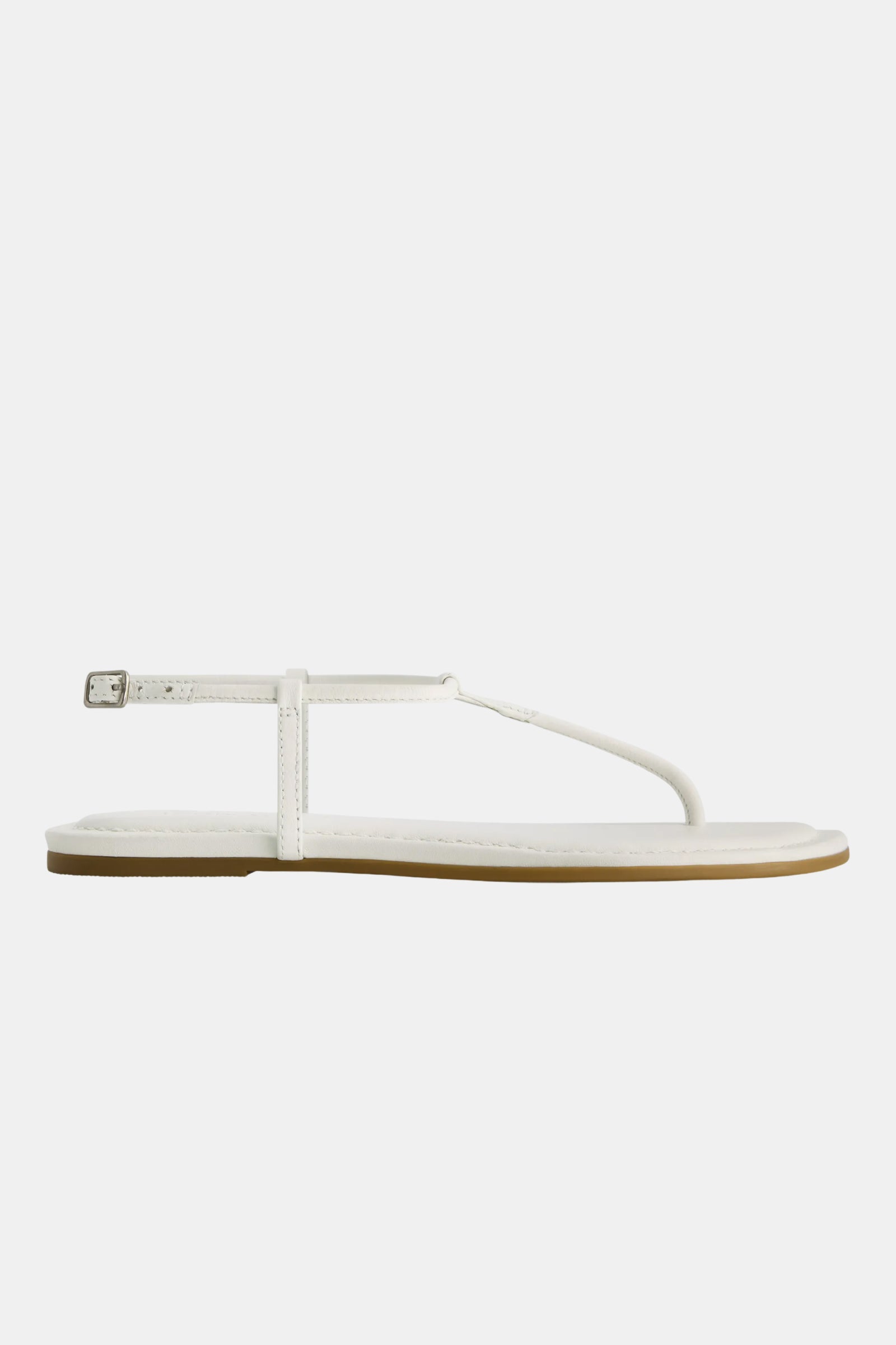 The Hercu Sandal is a minimalist white flat with a thin sole, simple thong strap, and an ankle strap with a small buckle, shown from the side on a plain white background.