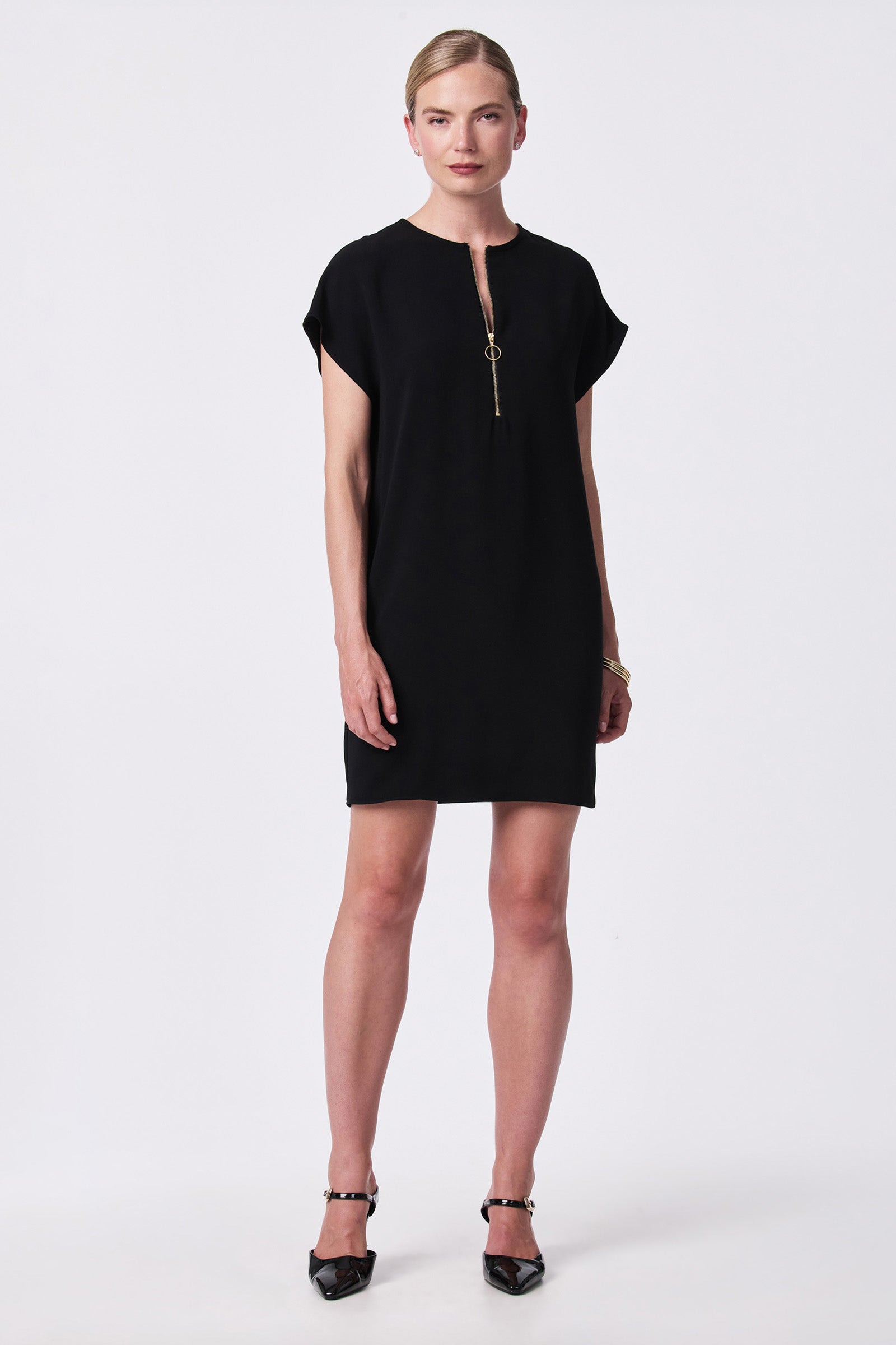 A woman faces forward in the Hasil Short-Sleeve Shift Dress, featuring a front zipper, paired with black pointed-toe heels. Her hair is pulled back and she stands against a plain white background.