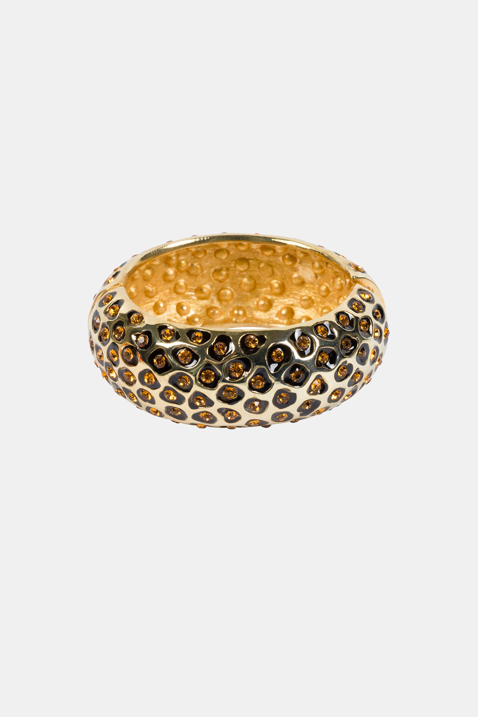 The Topaz Leopard Bangle is a gold ring with a rounded shape, raised hexagonal patterns filled with small brown stones, and a dotted texture on the interior. The background is plain white.