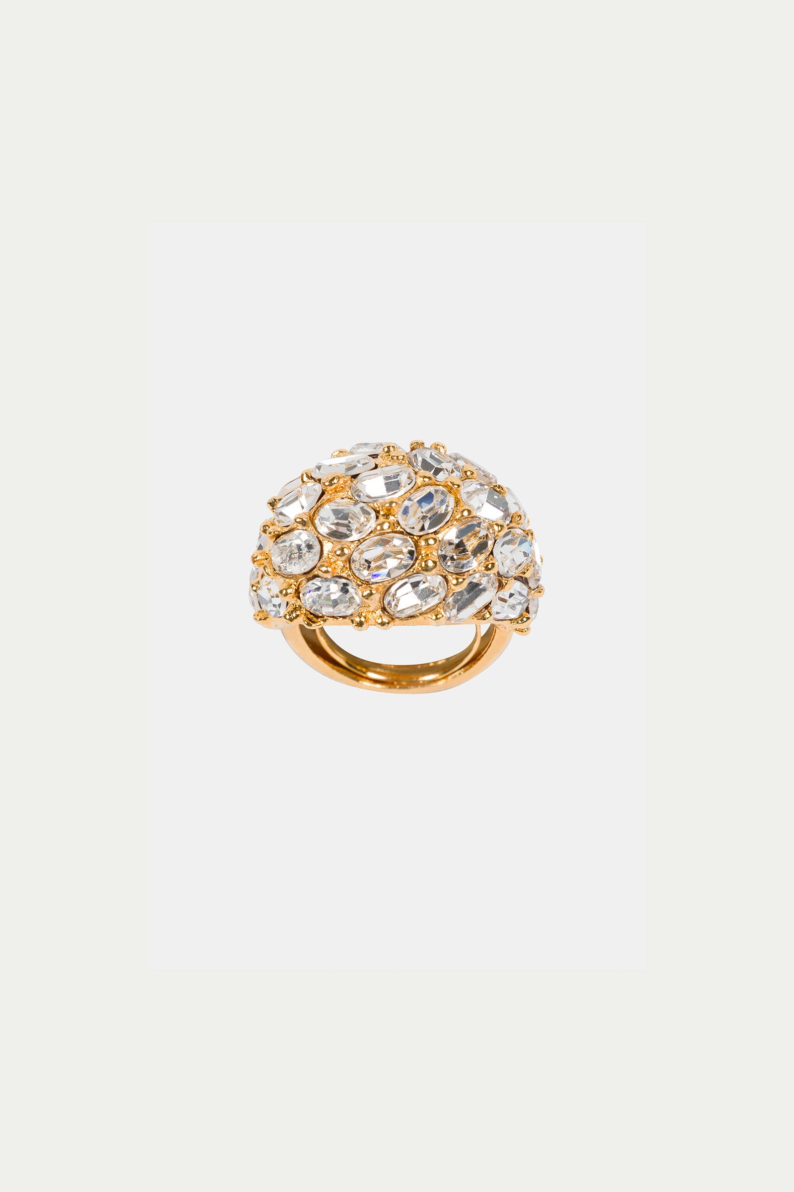 The Cluster Stone Dome Ring is a gold ring with a domed top, showcasing an intricate openwork design and multiple clear, oval and round gemstones. Its luxurious, ornate appearance stands out against a plain white background.