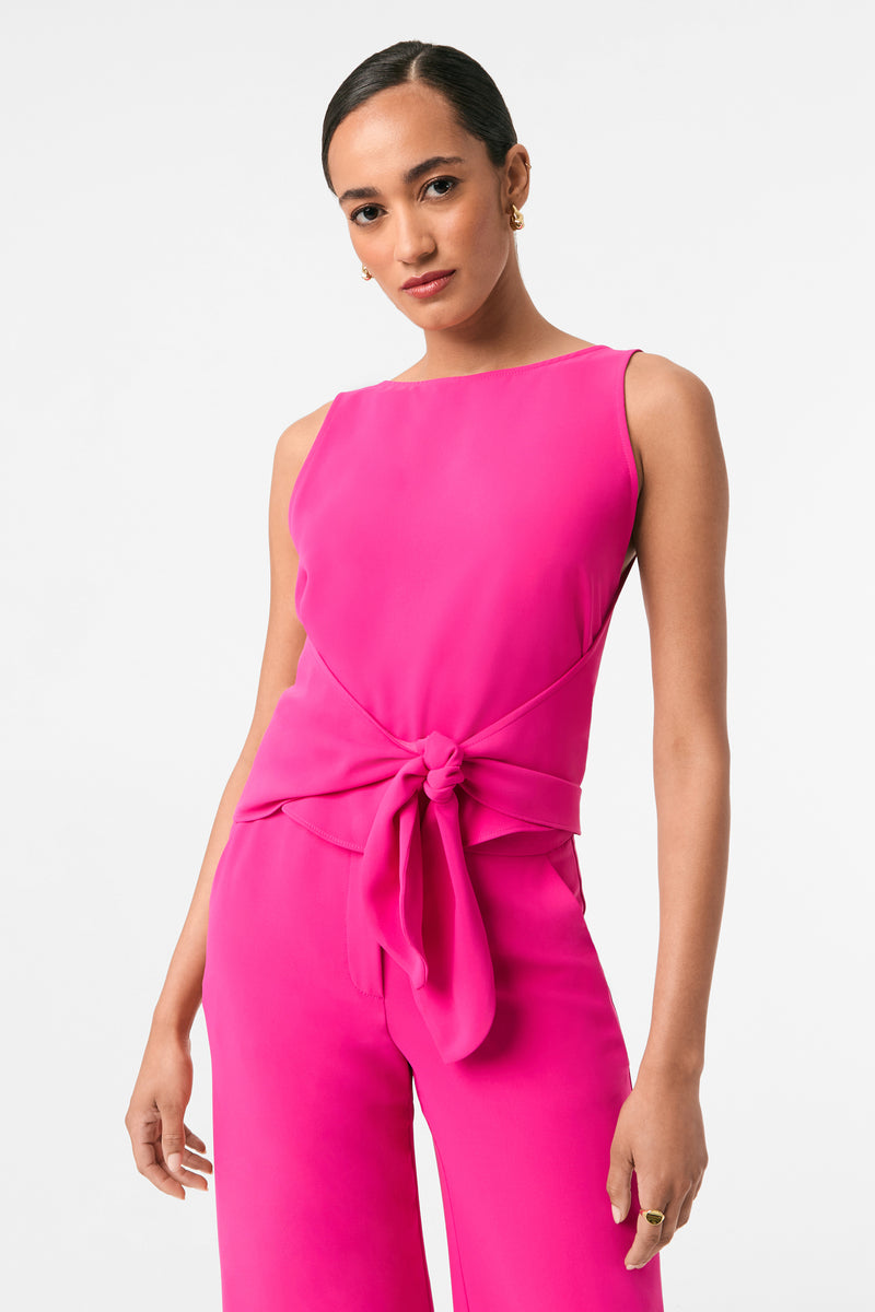 Woman wearing a bright pink jumpsuit with a tie detail on a white background