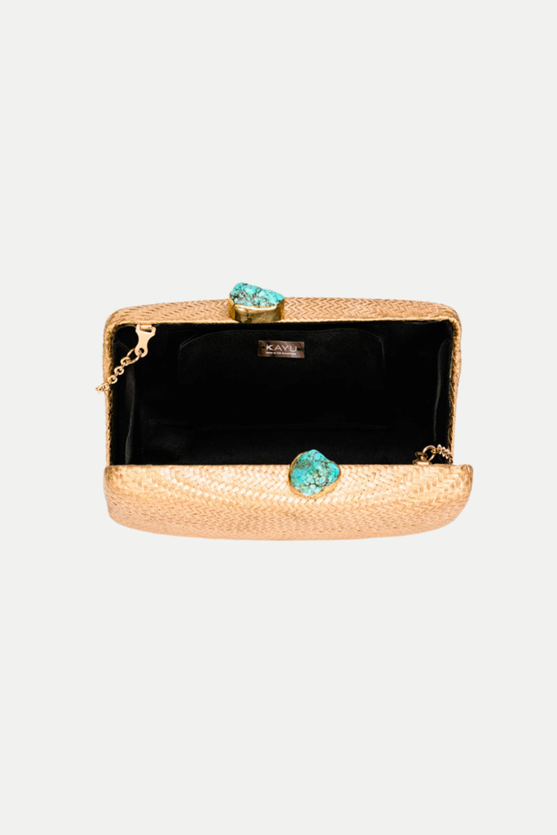 The Jen Gold Straw Clutch with Turquoise Closure features a textured gold exterior, black interior, chain strap, interior label, and a clasp adorned with two turquoise gemstone accents.