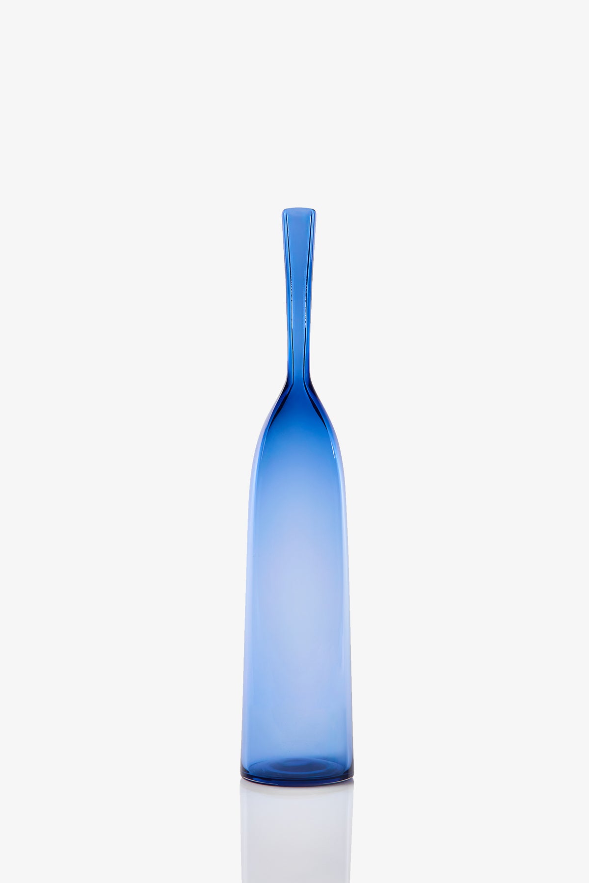 A Large Angelic Bottle stands tall and slender, crafted from blue glass with a long narrow neck. Set against a plain white background, its smooth, minimalist design is accentuated by a subtle reflection beneath it.