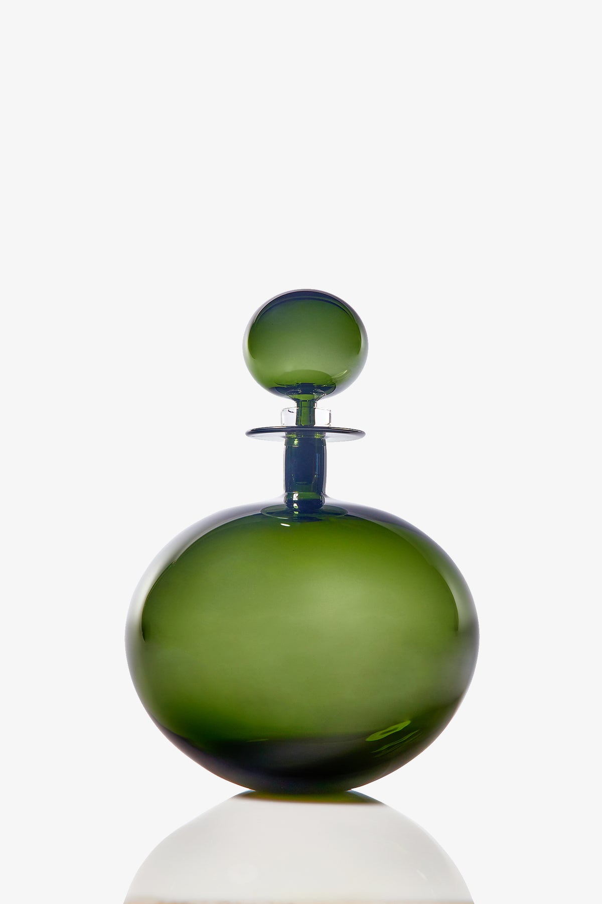 A Large Low Round Decanter made of green glass, featuring a matching spherical stopper, is displayed against a white background. The decanter casts a soft reflection on the surface below.