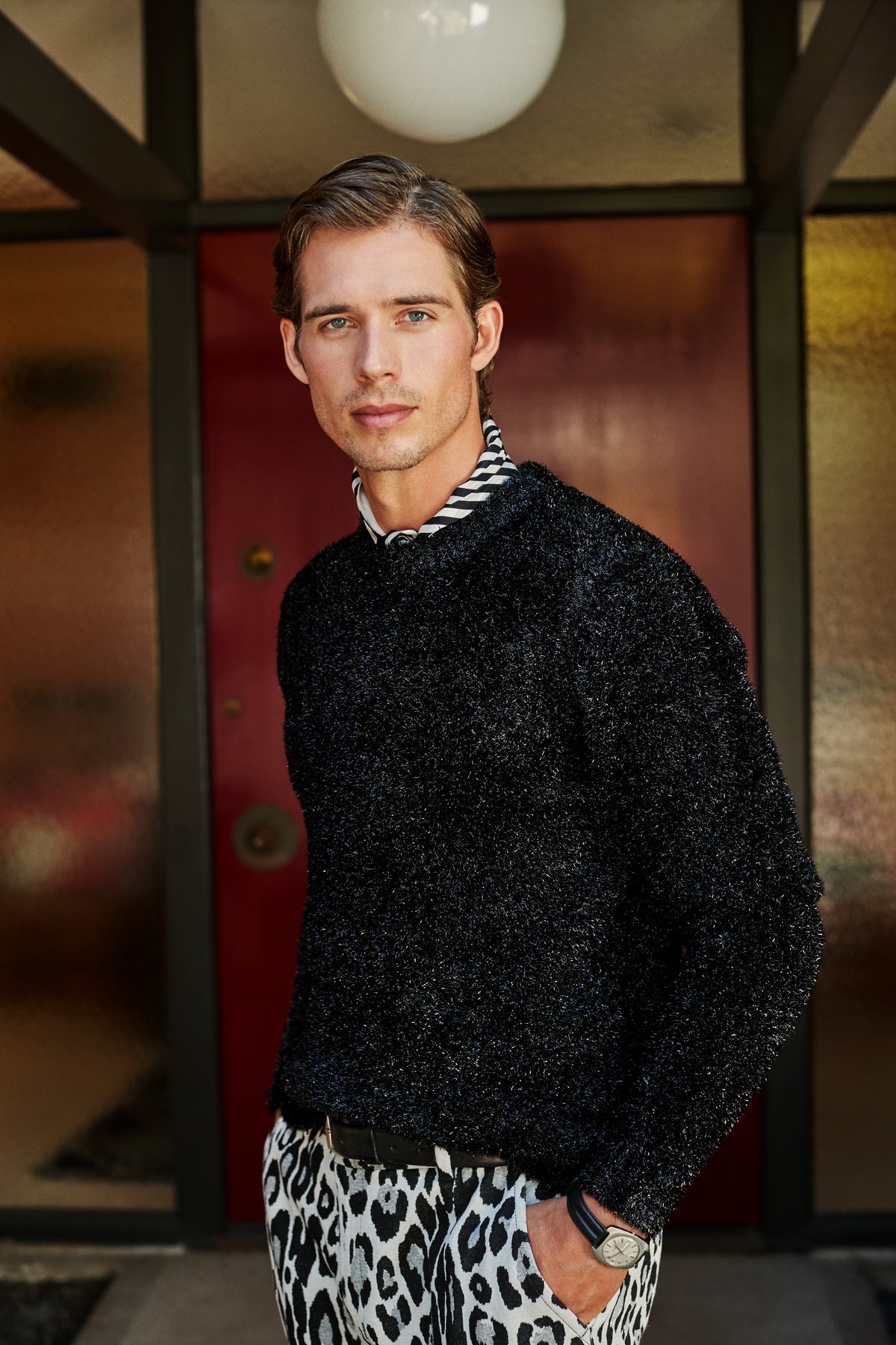 A man wearing an ASTRON SPARKLE CREWNECK over a black and white striped shirt and leopard-print pants.