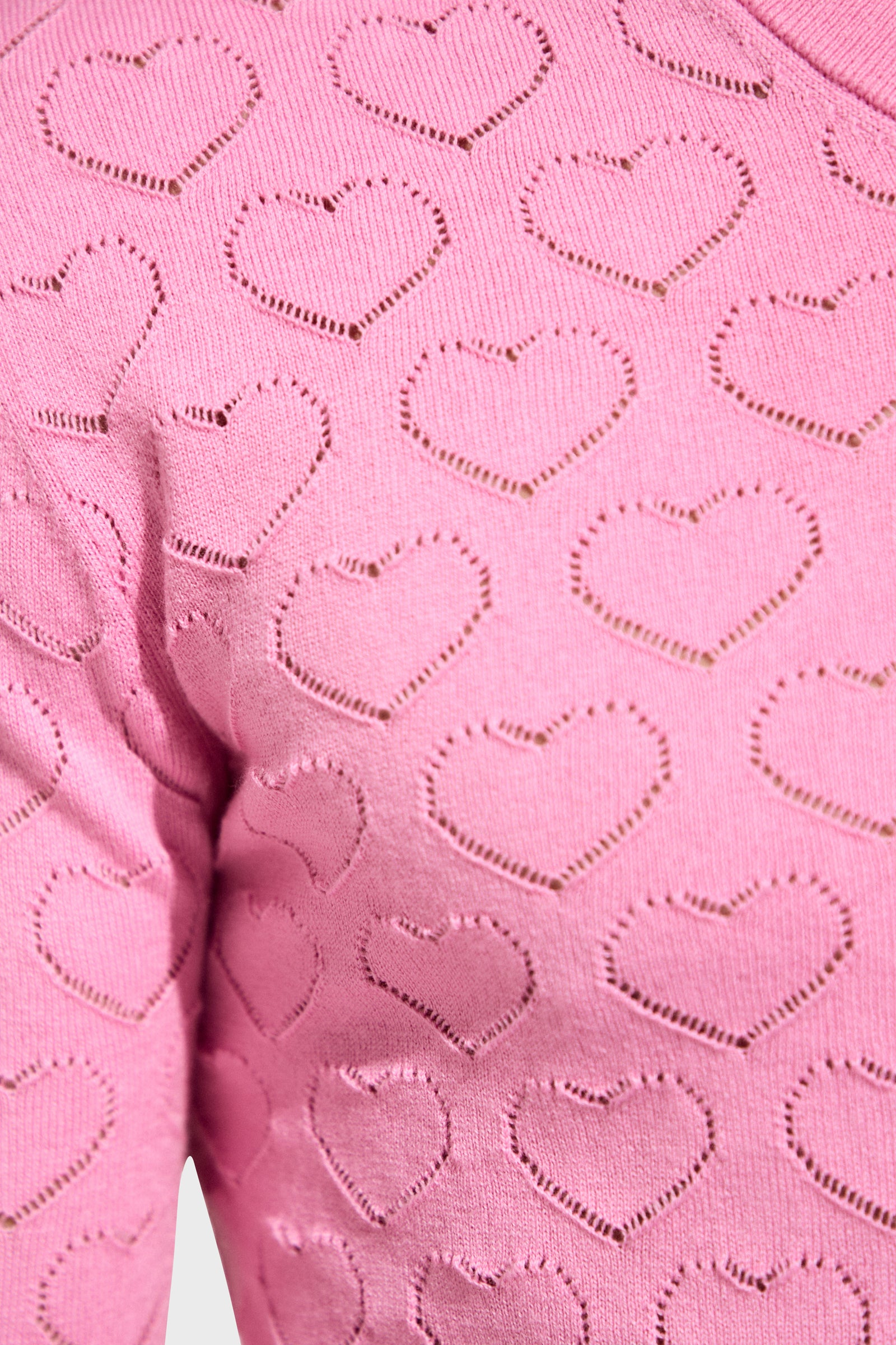 Close-up of Eros Heart Pointelle, a pink knitted fabric with a repeating pattern of heart-shaped cutouts.