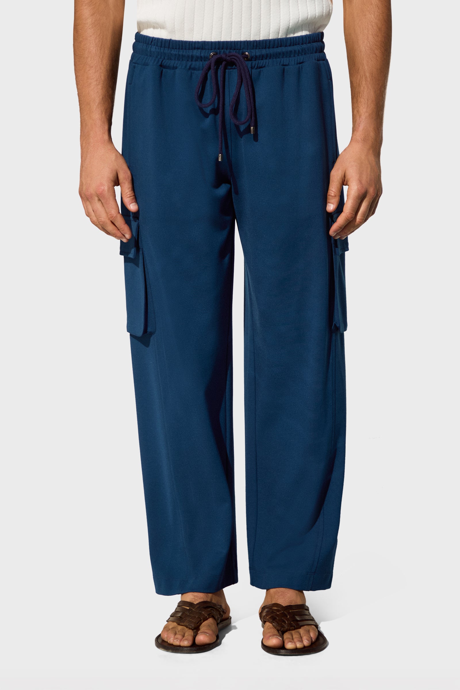 Someone wearing Lounge Cargo Pants in a loose fit with side pockets, paired with a white ribbed top and brown sandals, stands against a plain white background.