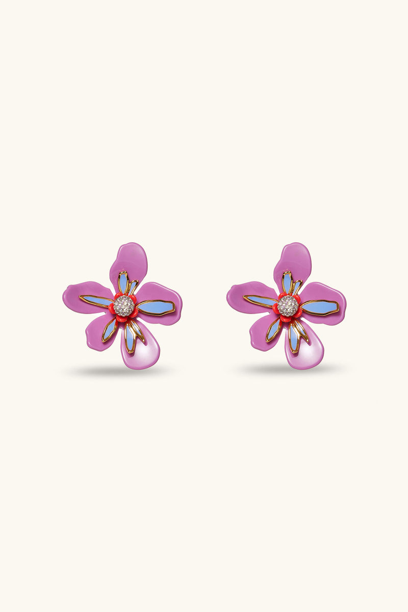 The Lele Sadoughi x Trina Turk Soie Paradis Earrings are magenta, flower-shaped with gold outlines and orange centers, shown against a light beige background.