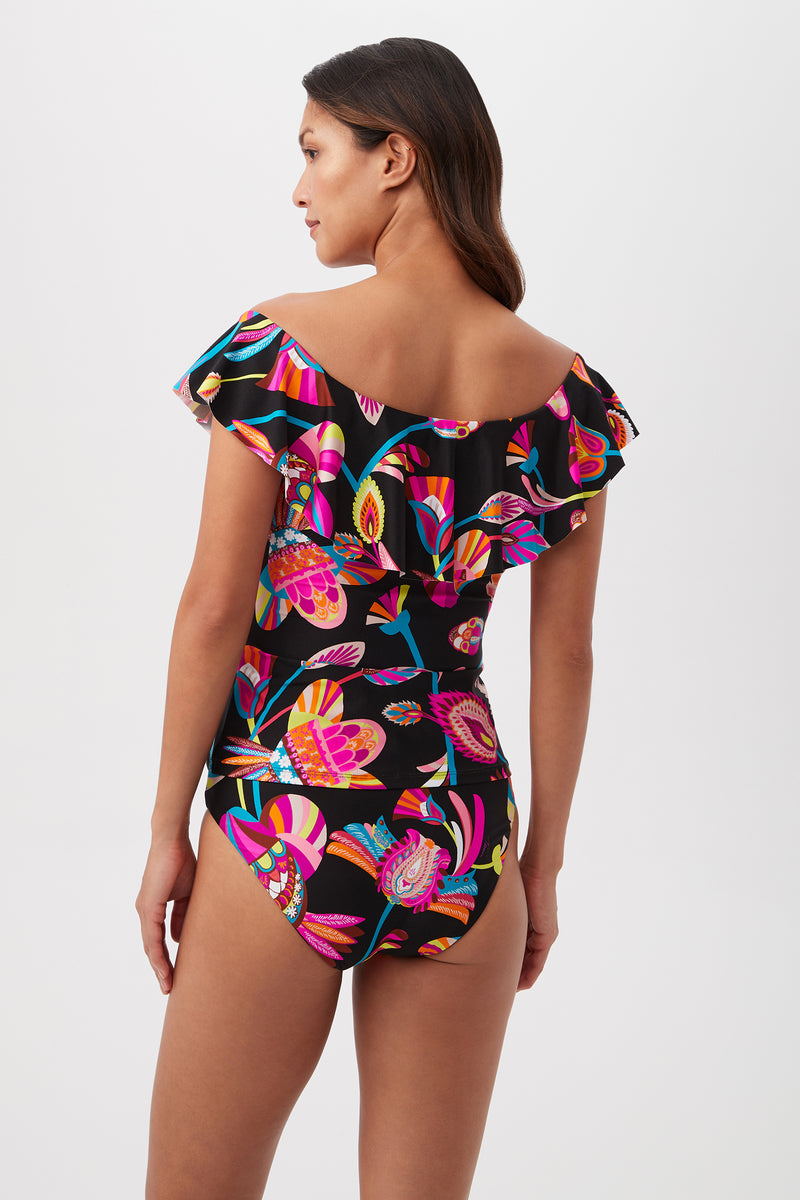 A woman with long brown hair models the Luminary Off-the-Shoulder Ruffle Tankini Swim Top, featuring a vibrant floral and leaf print, shown from the back against a plain white background‚Äîan eye-catching swimwear piece.