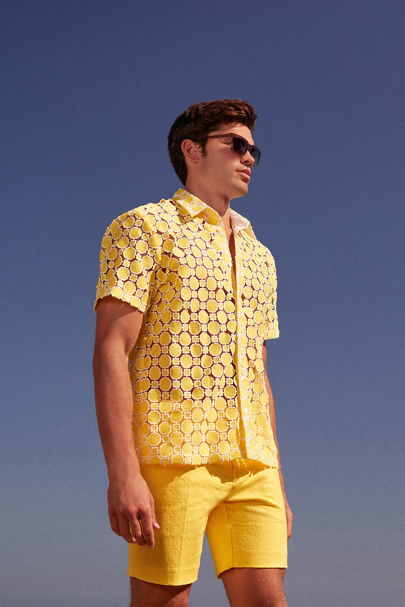 A man in the Long Beach Short-Sleeve Shirt, sunglasses, and matching yellow shorts stands outdoors beneath a clear blue sky.