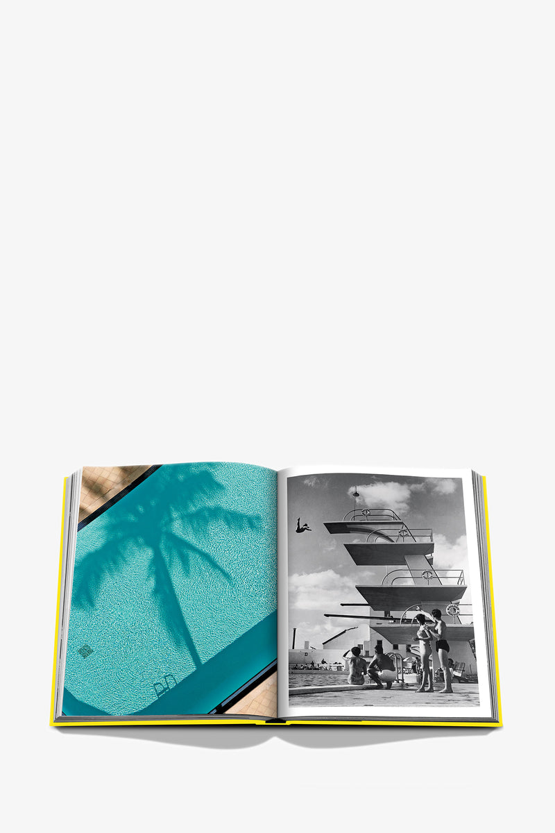 An open Assouline Miami Beach Book displays a color photo of a pool with palm shadows on the left page and a black-and-white image of people at a diving platform on the right page.