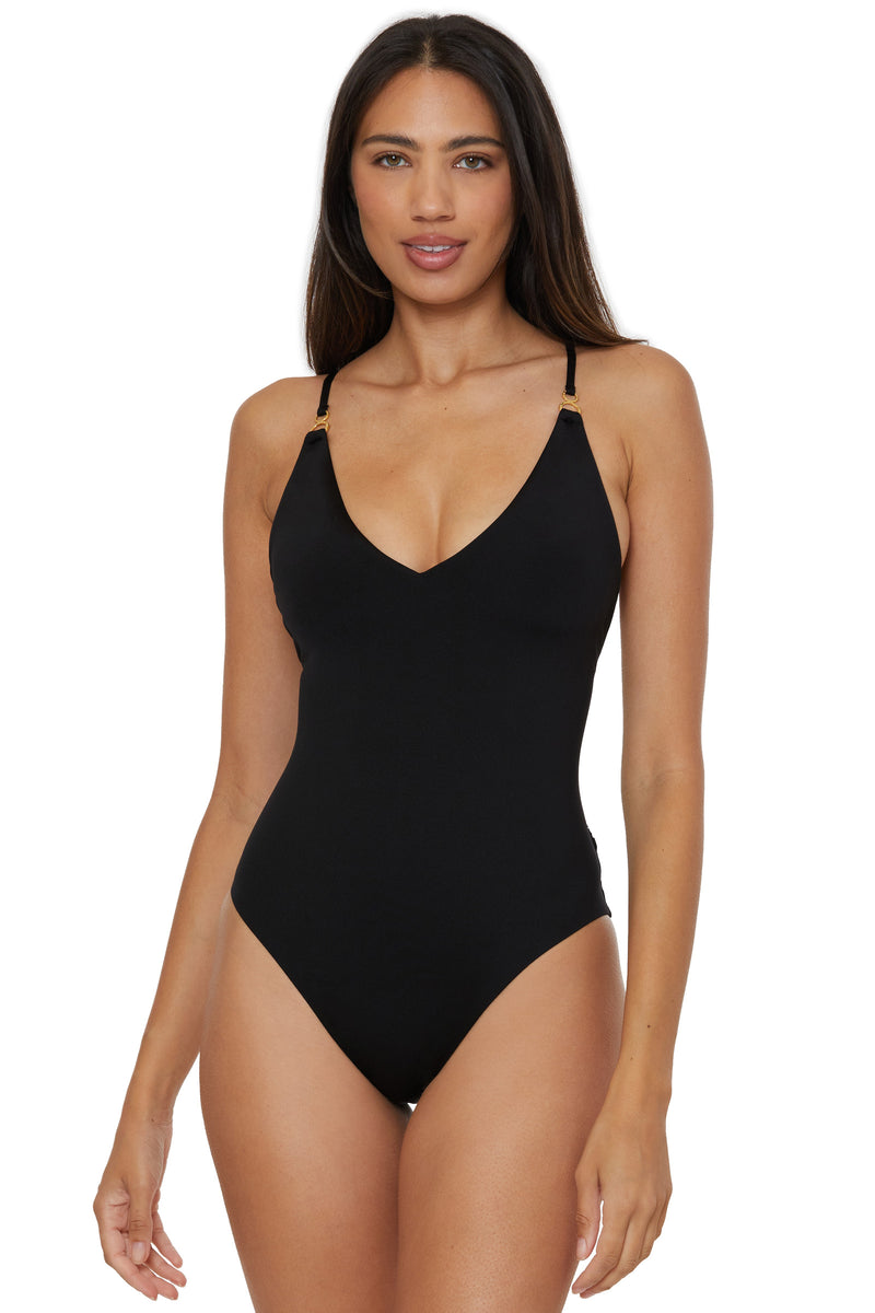A woman with long dark hair is wearing the Monaco Twist Back One-Piece Swimsuit in black, featuring thin straps and a V-neckline, standing against a white background.