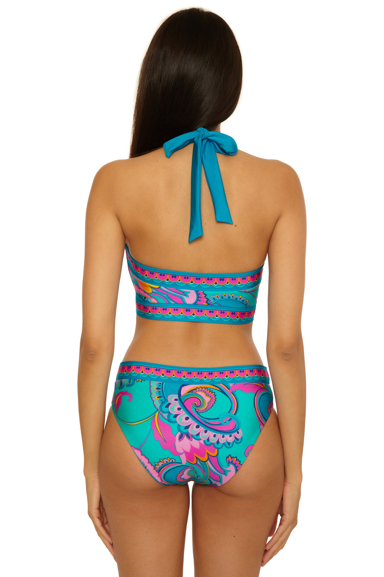 A woman with long brown hair is seen from the back, wearing the Mykonos Reversible Hi Neck Top featuring a blue base with a colorful paisley pattern in pink, turquoise, and purple.