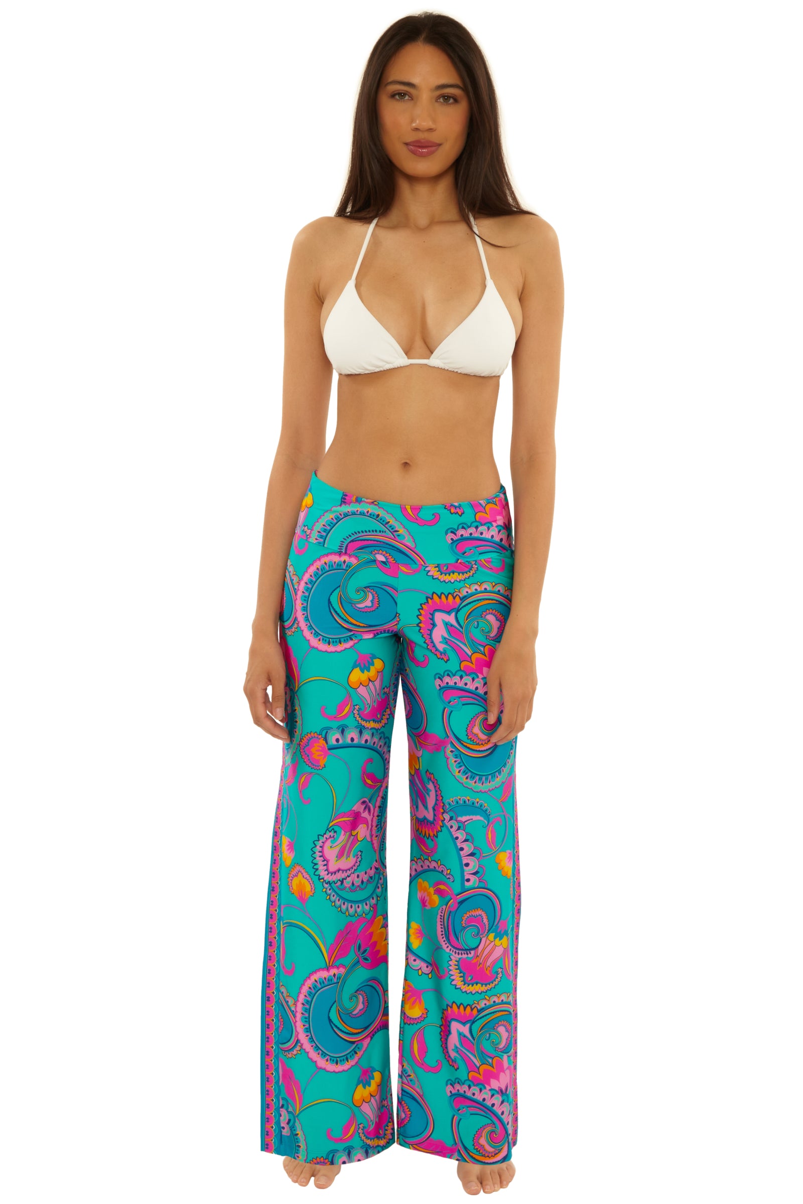 A woman faces forward wearing a white bikini top and the Mykonos Border Swim Pant—teal high-waisted, wide-leg pants with a colorful paisley pattern in pink, purple, yellow, and blue.