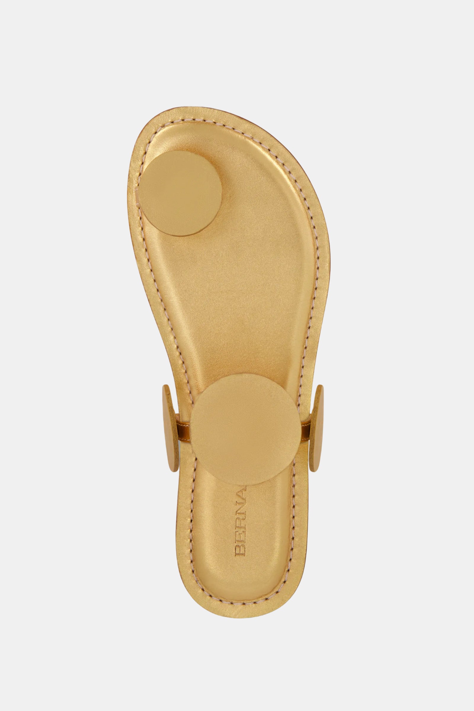 The Bernardo New Moon Sandal is a tan leather sandal featuring three large round gold-toned discs—at the toe, mid-foot, and sides. Displayed on a plain white background, the insole shows the BERNA brand name.