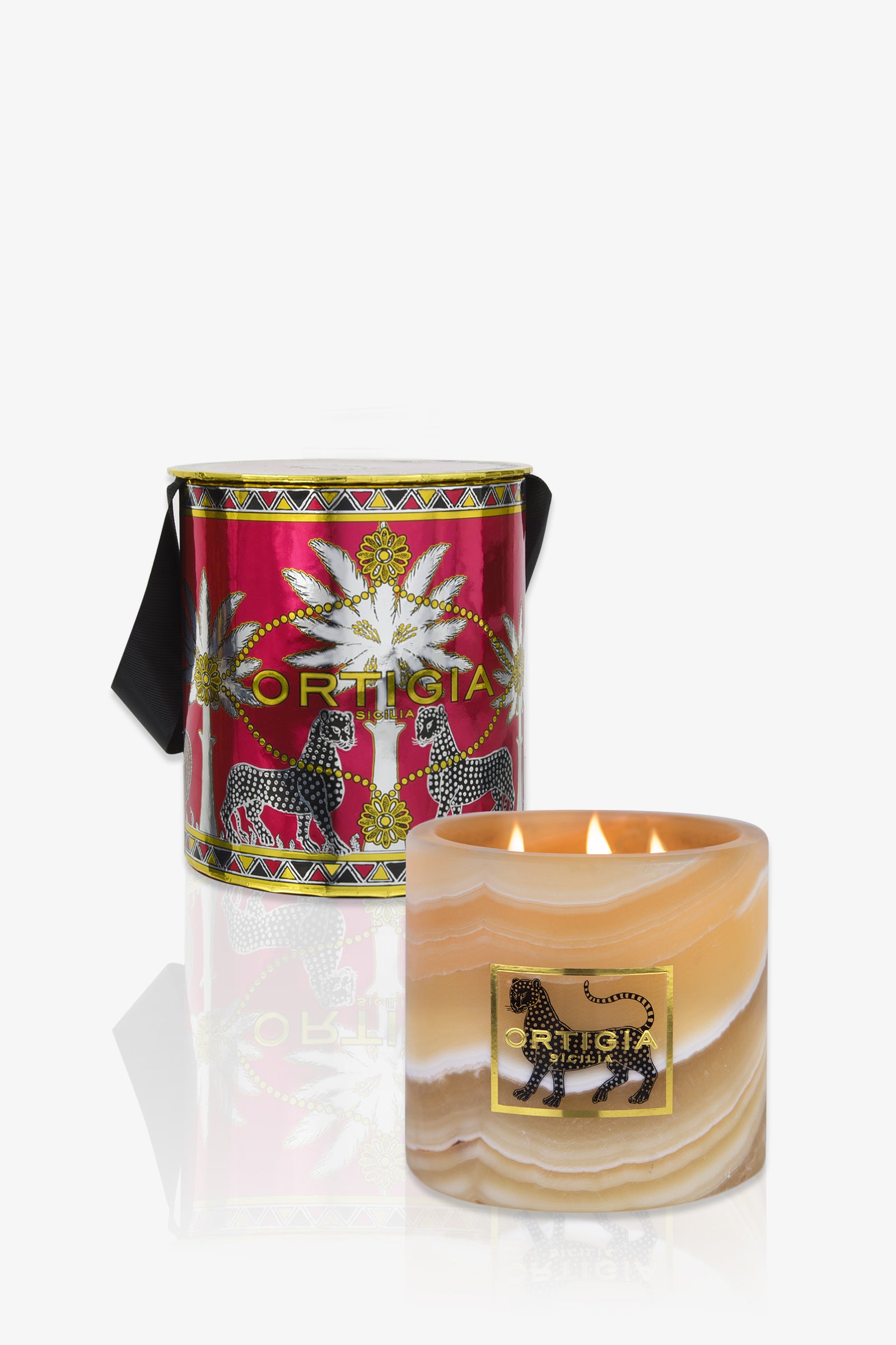 The Ortigia Ambra Nera Alabaster Small features a marbled holder with a black leopard design, placed before a red and gold Ortigia box decorated with palm trees and zebras on a white background.