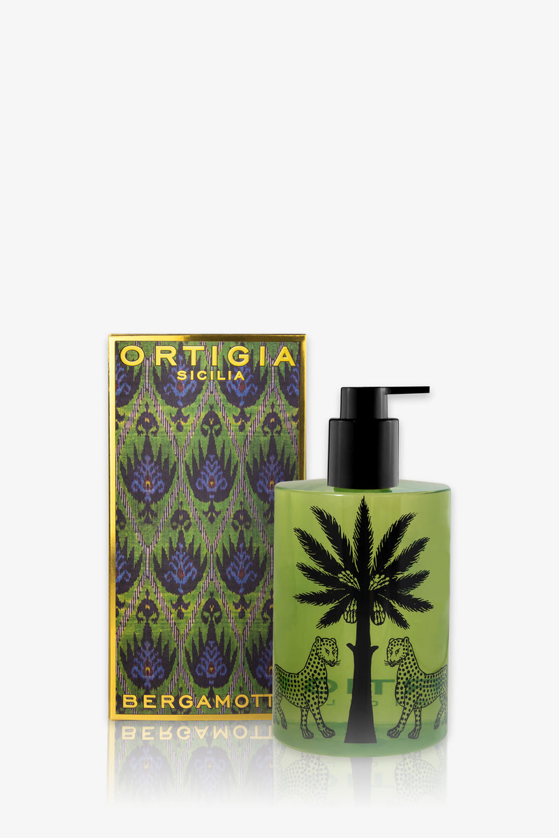 A green Ortigia Bergamot Shower Gel bottle with a black pump, featuring two black leopards and a palm tree, is displayed beside its colorful patterned box.