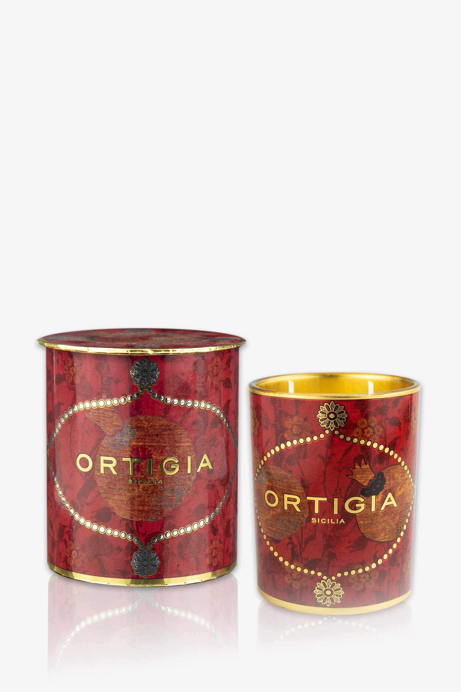 The Ortigia Melograno Medium Candle features red and gold decorative packaging with an ornate pattern, displayed alongside its matching candle jar and cylindrical box, both highlighted with elegant gold accents.