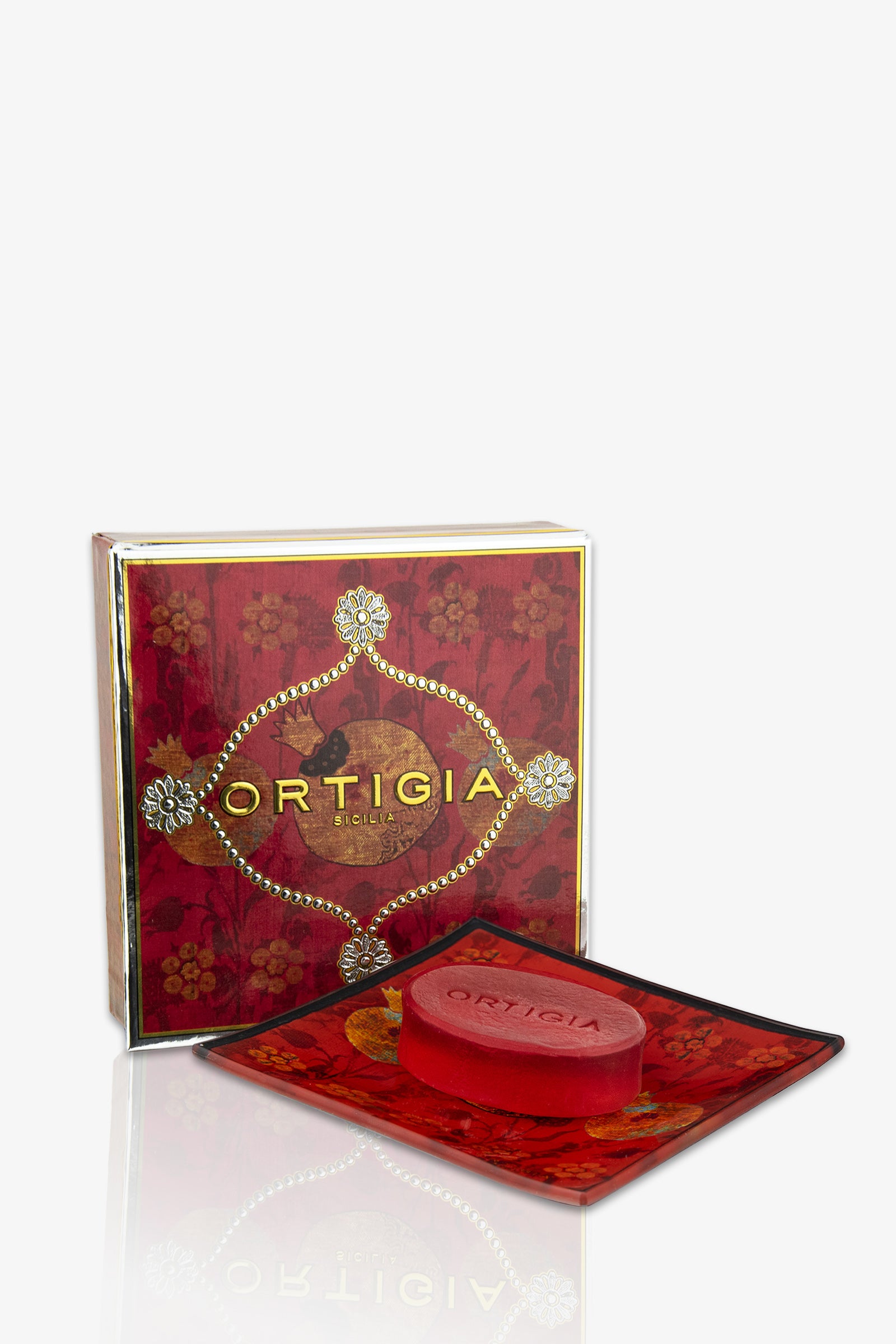 An Ortigia Melograno Soap Plate, featuring a red soap on a matching decorative dish, is displayed in front of an ornate red and gold floral-patterned Ortigia gift box.
