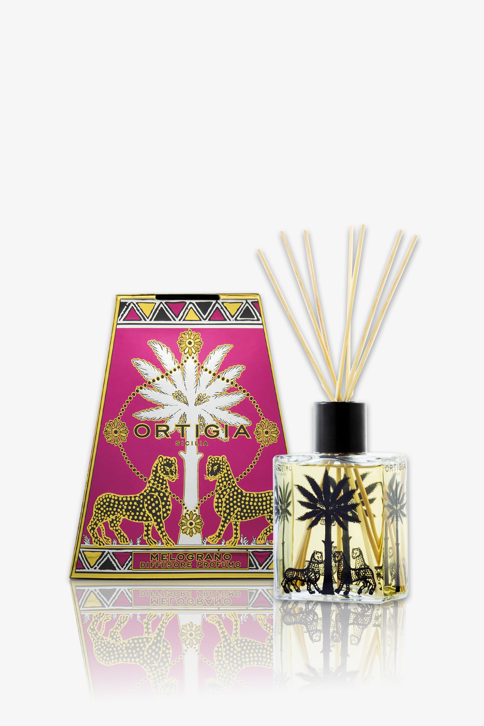 The Ortigia Melograno Diffuser features a clear bottle with black palm tree and leopard designs, filled with reed sticks, and comes in a matching pink and gold box with palm tree and leopard motifs.