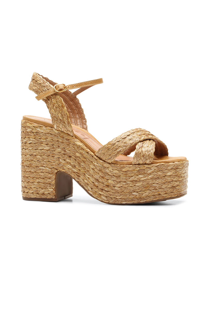 The Garda Platform is a NATURAL woven sandal featuring a chunky heel, braided straps, an ankle buckle closure, and a straw-like material.