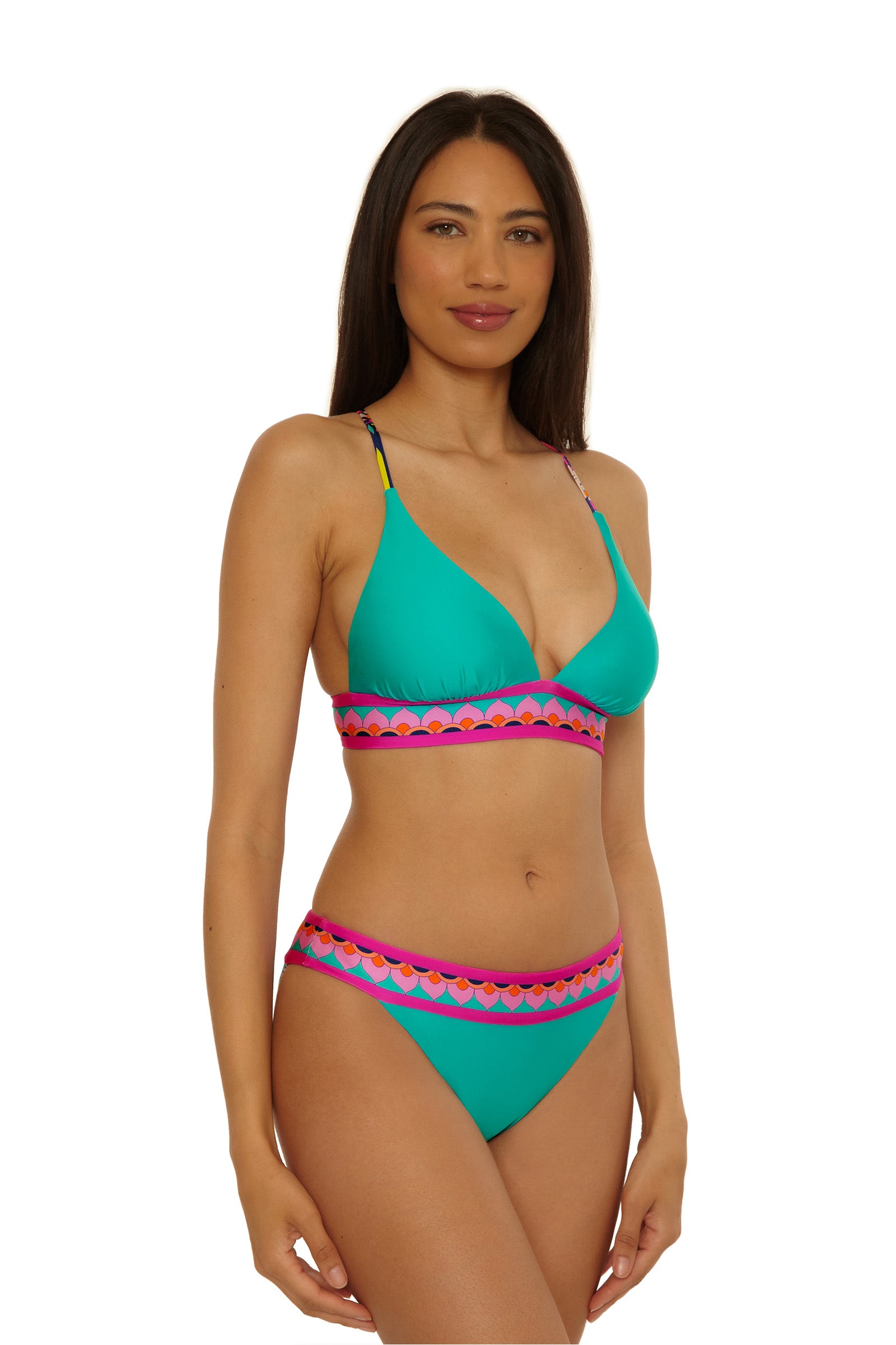 A woman with long dark hair models the Paralia Reversible Halter Top, a teal bikini with a pink and orange geometric band on the bra and waistband. She stands in front of a plain white background, looking at the camera with a slight smile.