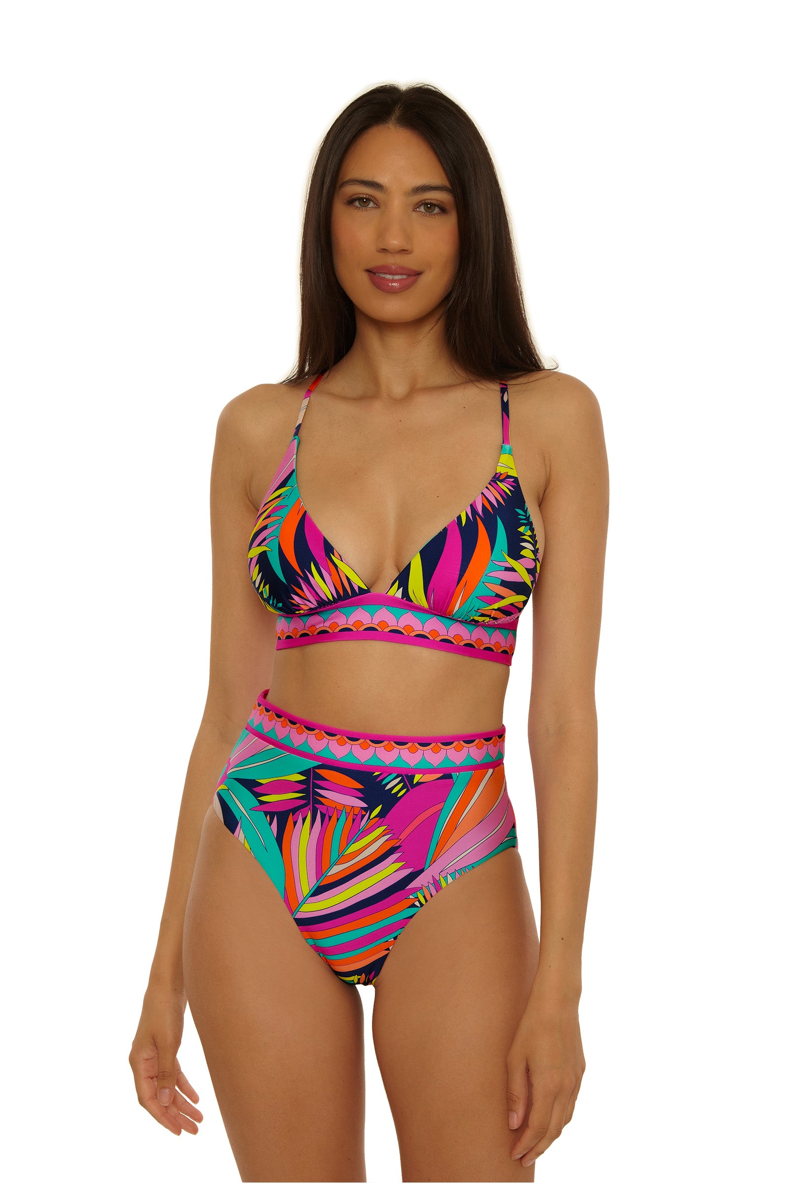 A woman with long dark hair wears the Paralia Rev Hi Waist Bottom bikini with a strappy tropical-print top, standing and smiling slightly against a plain white background.