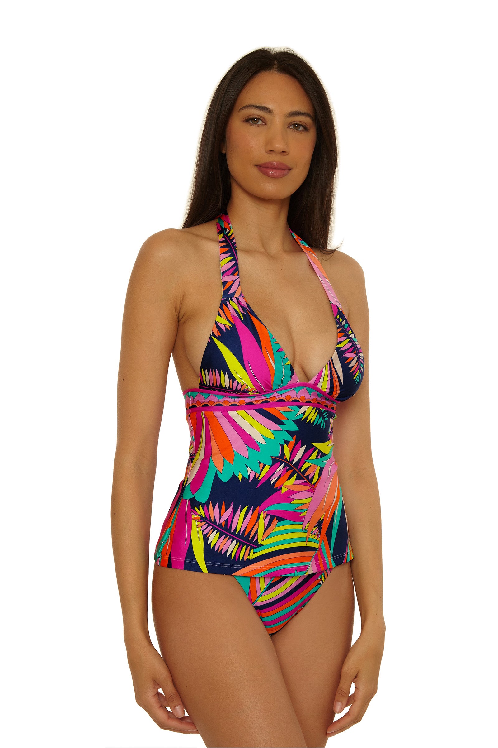 A woman wears the Paralia Banded Tankini, a colorful halter-neck swimsuit with a vibrant abstract feather pattern in pink, blue, yellow, and green, standing and facing forward against a plain white background.