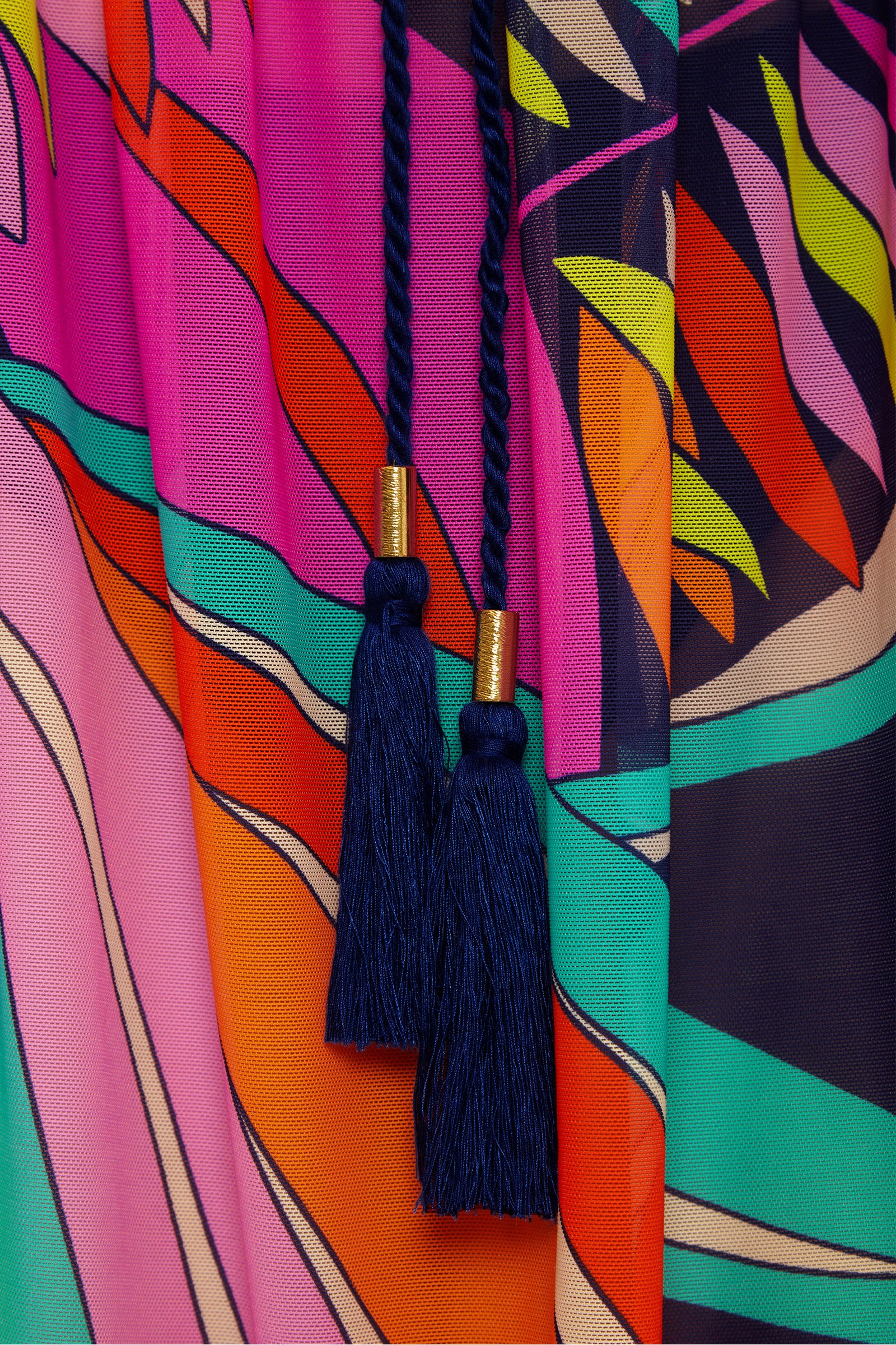 Close-up of the Paralia Mesh Tunic Dress featuring colorful, bold stripes in pink, orange, teal, and navy. Two dark blue braided cords with tassels and gold details hang down the center.