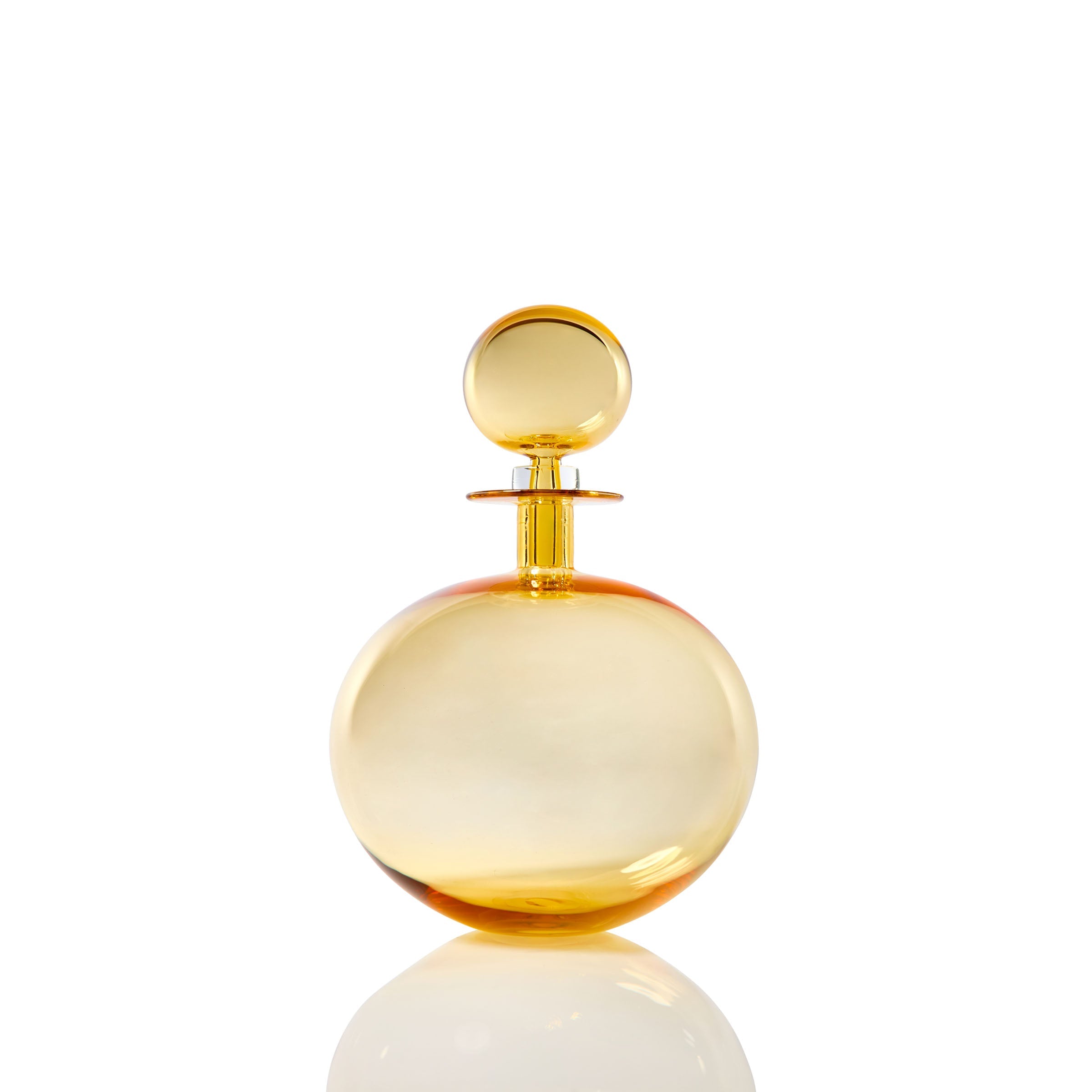 The Petite Low Round Decanter in whiskey, featuring an elegant silhouette and matching spherical cap, is showcased against a white background with a subtle reflection below.